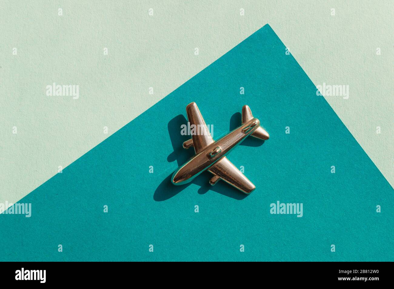 Metallfigur des kleinen Flugzeugs auf dem Turqouise- und hellblauen Geometriehintergrund. Flatlay, Draufsicht, Layout. Luftfahrtindustrie Stockfoto