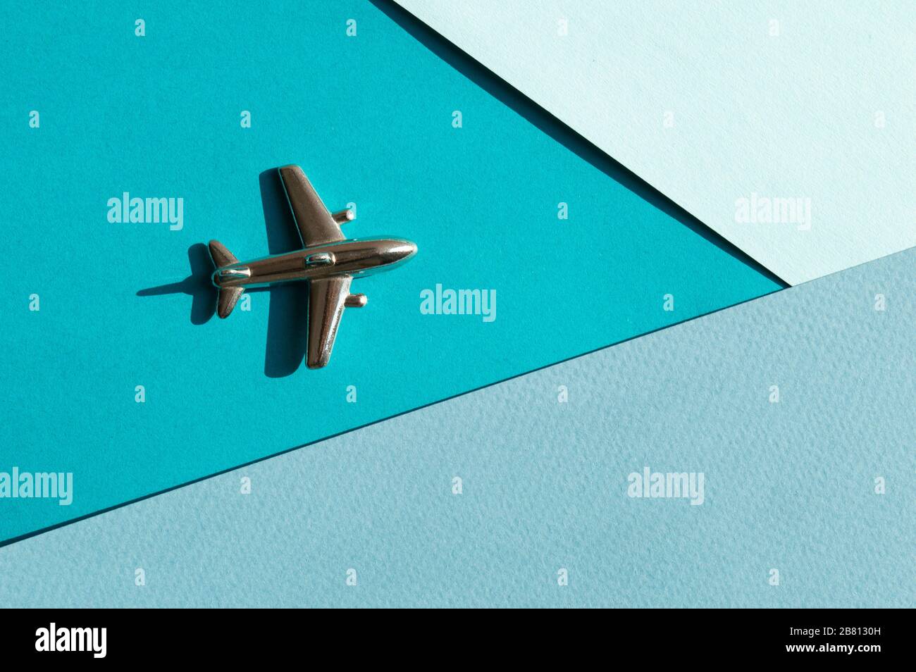 Metallfigur des kleinen Flugzeugs auf dem Turqouise- und hellblauen Geometriehintergrund. Flatlay, Draufsicht, Layout. Luftfahrtindustrie Stockfoto