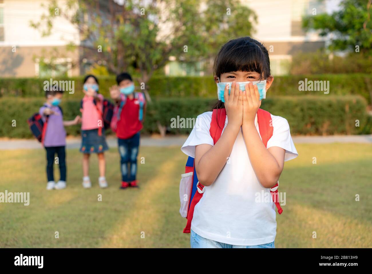 Asiatische Mädchen Vorschulkinder Schüler mit gesunder Gesichtsmaske niesen mit Freunden im Hintergrund. Die Weltgesundheitsorganisation empfiehlt mindestens eine Stockfoto
