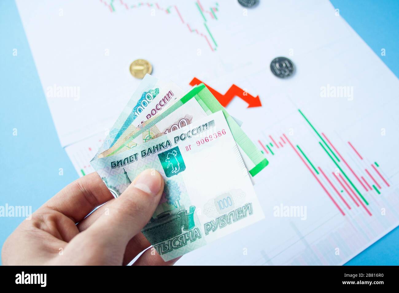 Männliche Hand, die Rubelrechnungen zum Wechselkurs des russischen Rubel und des roten Pfeils hält. Rubelabschreibung. Wechselkurs des Rubelfalls. Rubel zum Dollar Stockfoto