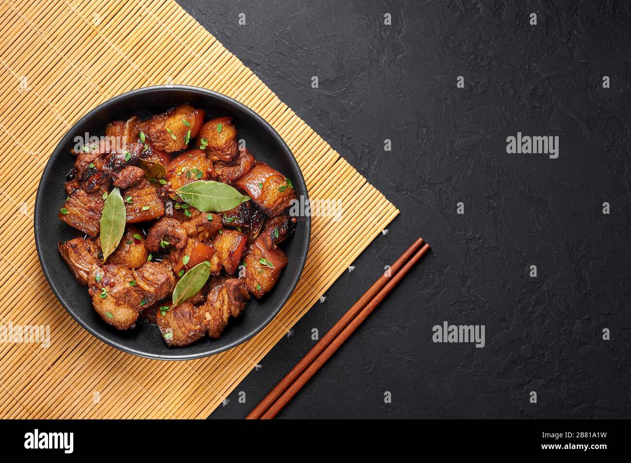 Adobo Schweinefleisch in schwarzer Schüssel im dunklen Schieferhintergrund. Schweineadobo oder Adobong Baboy ist ein philippinisches Gericht mit geschmortem Schweinebauch, Lorbeerblättern und Sojasoße Stockfoto