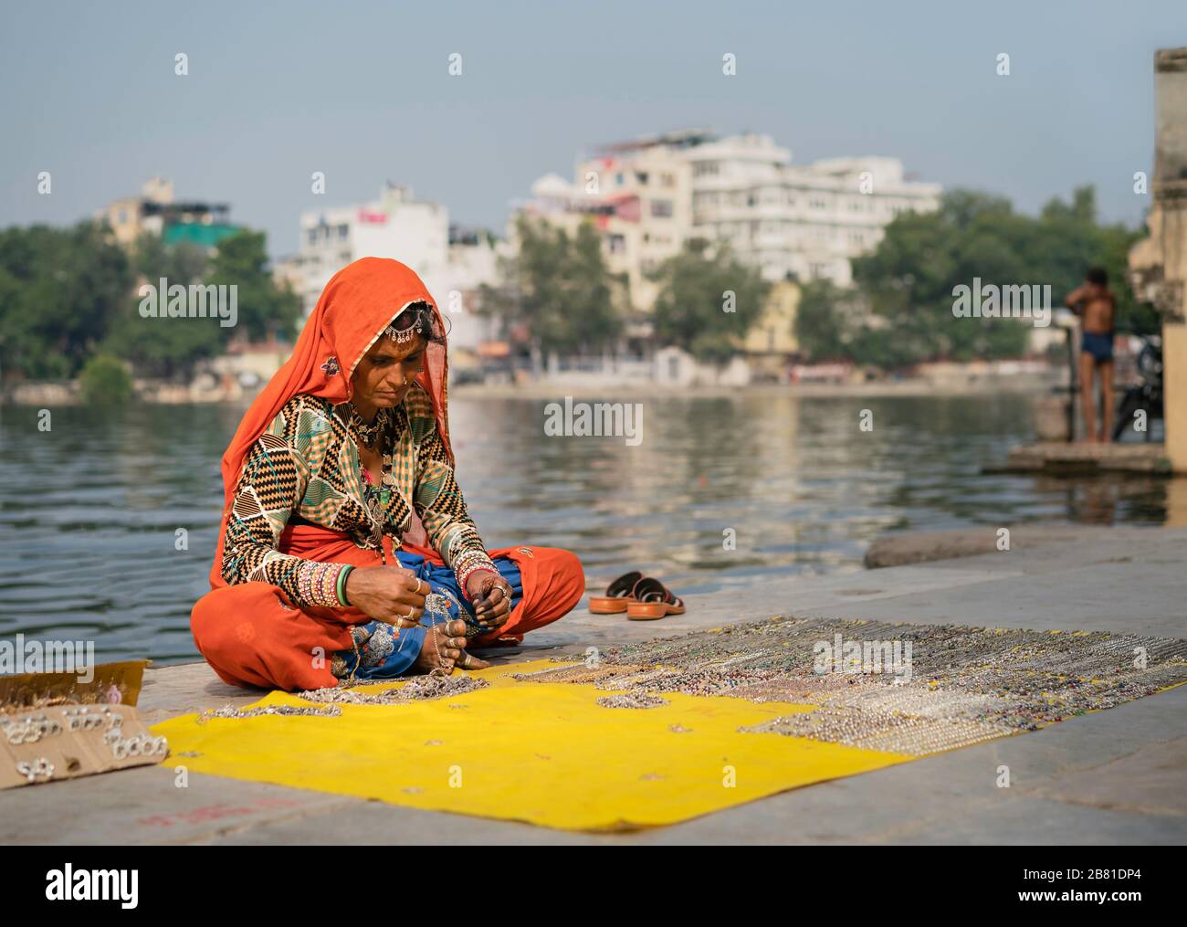Frau in traditioneller farbenfroher Kleidung verkauft ethnischen Schmuck neben der Seeufer am schönen Morgen in Udaipur, Rajasthan, Indien. Stockfoto