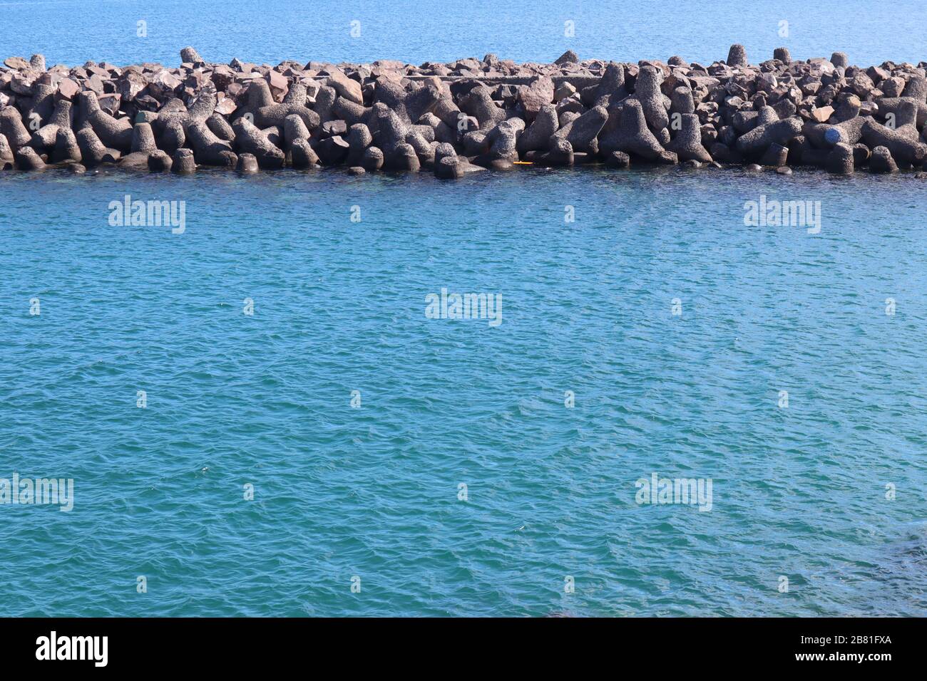 Wellenbrecher in einem ruhigen türkisfarbenen Meer mit klarem Himmel im Sommer Stockfoto