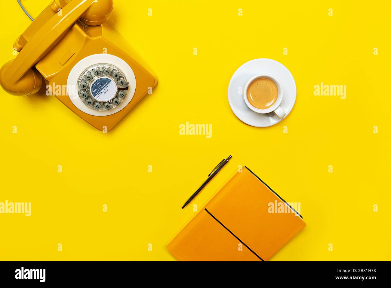Gelbes Layout mit Retro-Drehtelefon, Kaffeetasse, Stift und Notebook. Flaches Layout, Draufsicht, Kopierbereich. Stockfoto