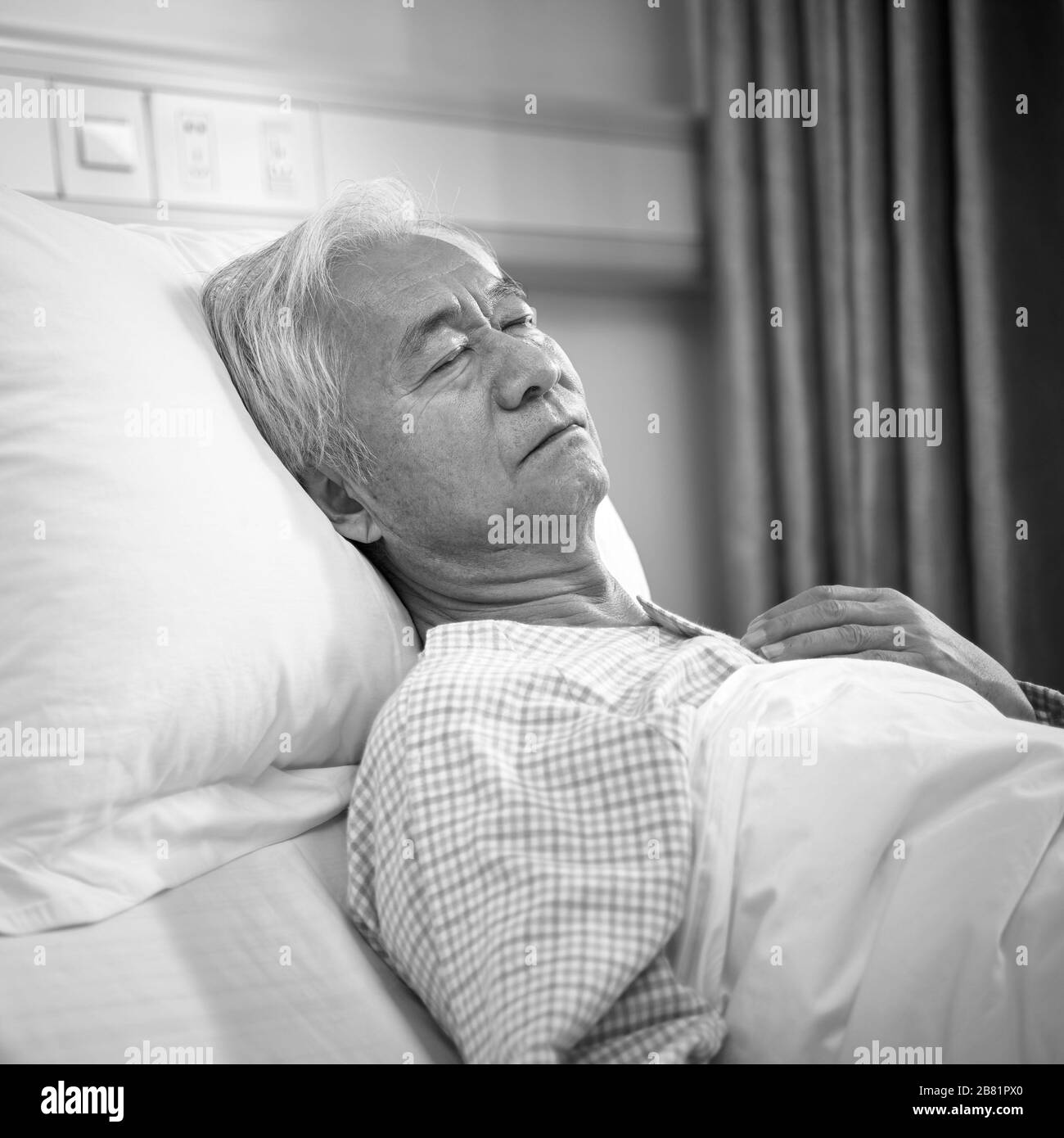 älterer asiatischer männlicher Patient, der im Bett liegt und in der Krankenstation oder der betreuten Wohneinrichtung schläft, schwarz-weiß Stockfoto
