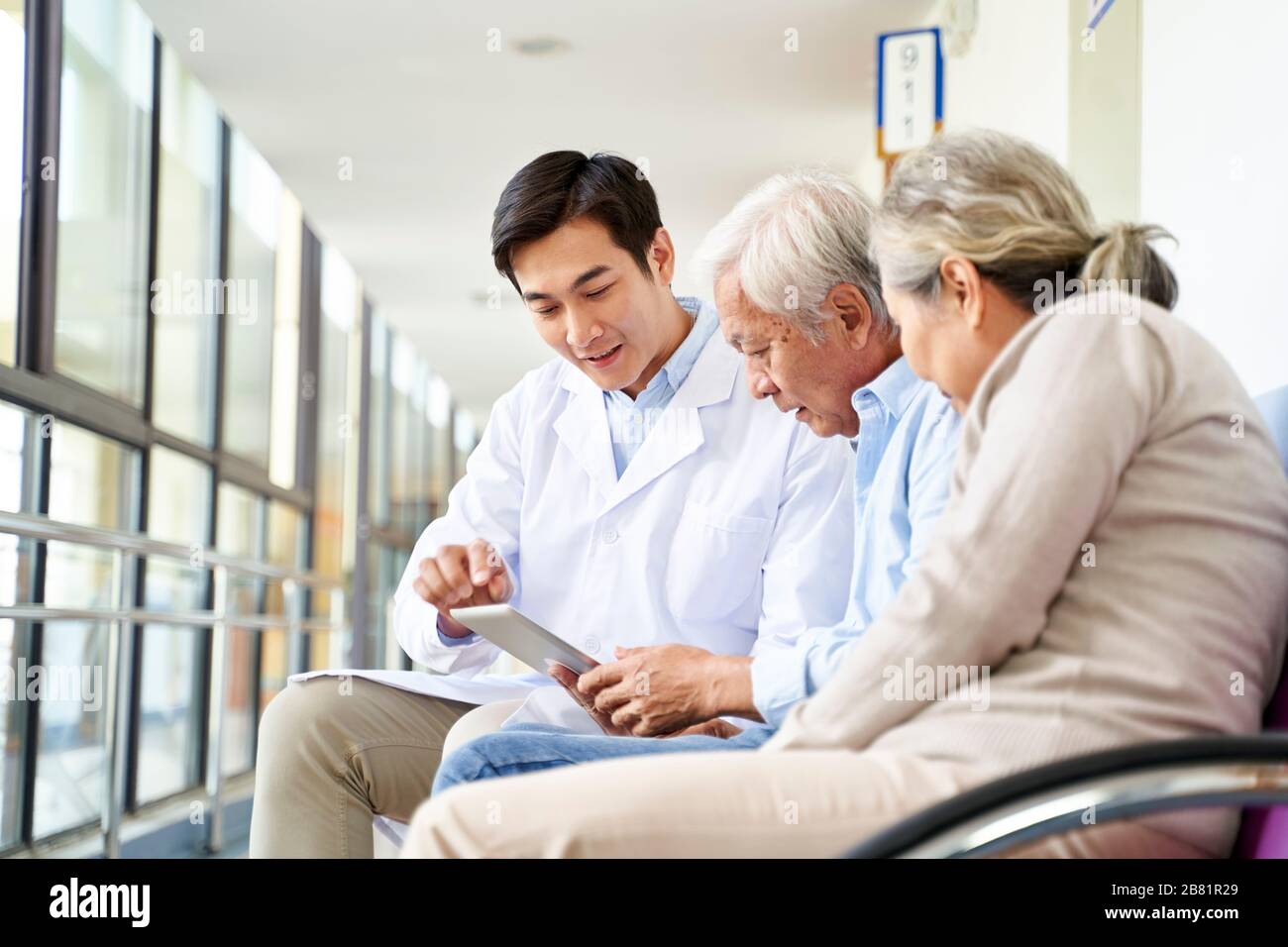 Junger asiatischer Arzt diskutiert Testergebnis und Diagnose mit älteren Paar-Patienten, die digitale Tablette im Krankenhausflur verwenden Stockfoto