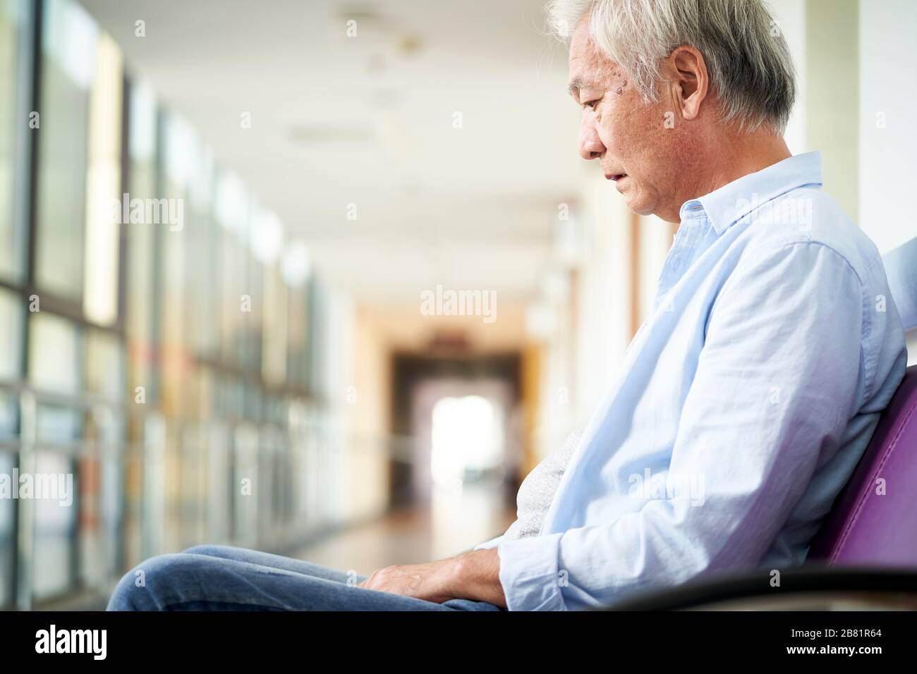 Trauriger und verwüsteter asiatischer Obermann, der allein im leeren Krankenhausflur sitzt, geht nach unten Stockfoto