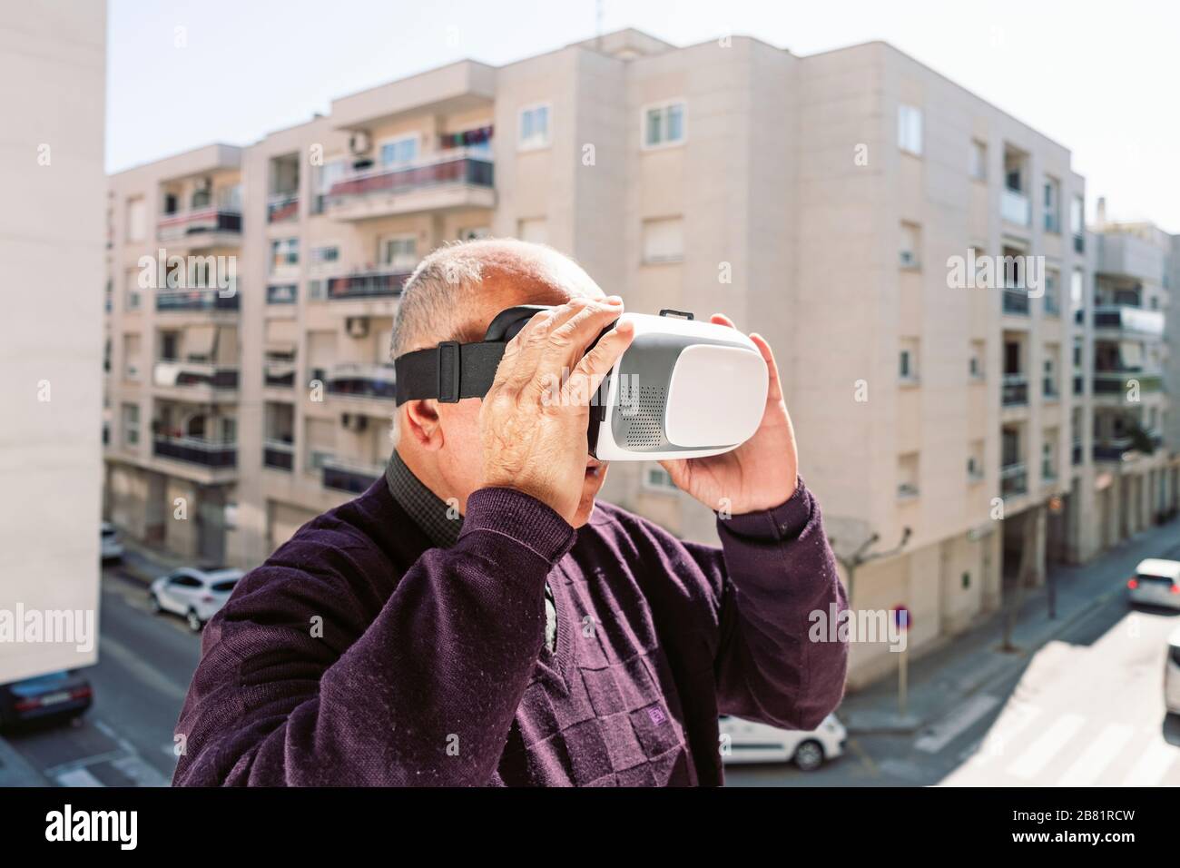 Nahaufnahme eines älteren kaukasischen Mannes mit einem Headset für virtuelle Realität im Freien vor einem Apartmentgebäude in einer ruhigen Stadt Stockfoto