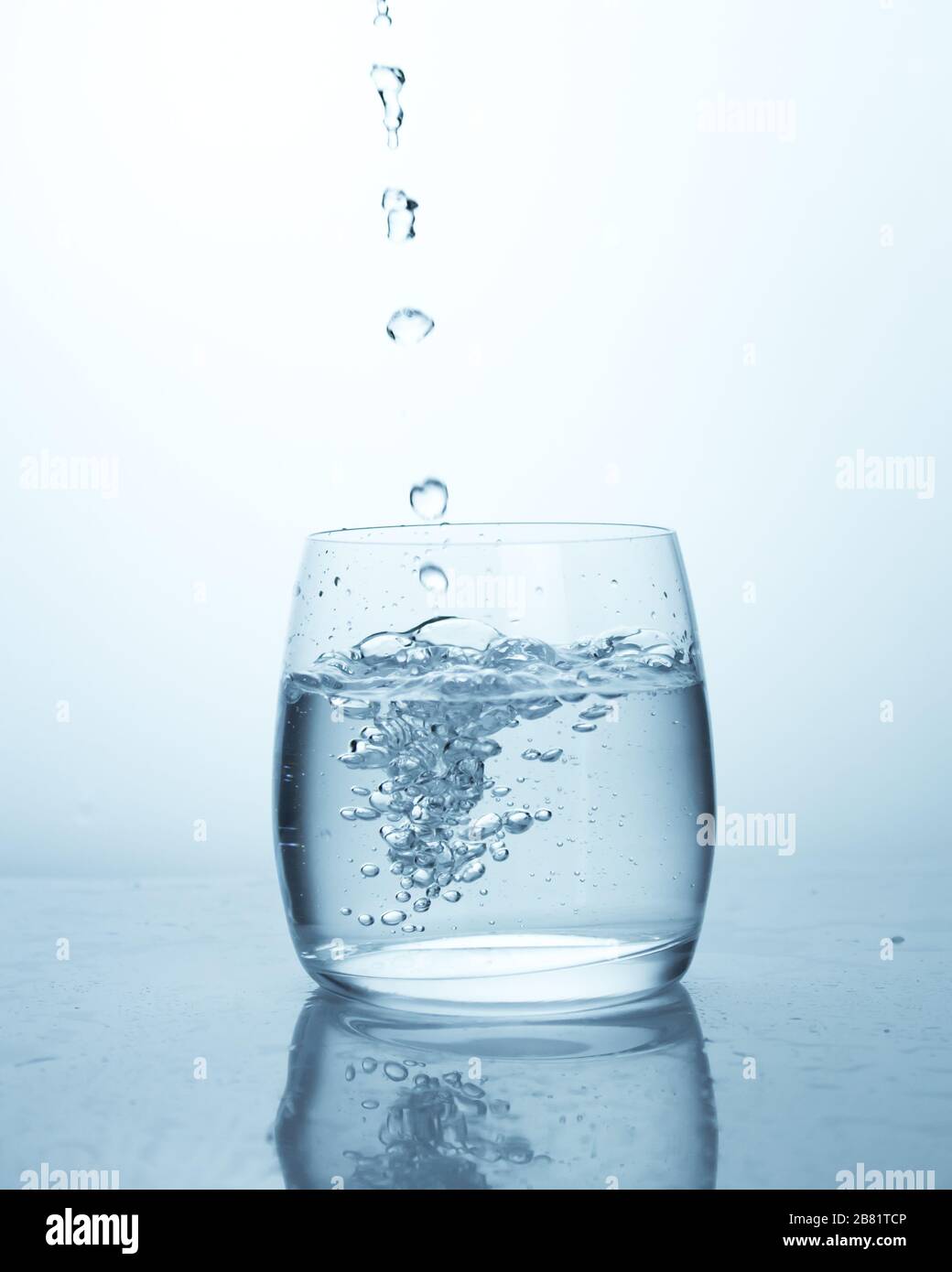 Wassertropfen, die in ein Glas Wasser fallen, schöne Blasen. Reines Quelltrinkwasser, das Durst abschrecken kann. Wasser mit Blasen in einem durchsichtigen Wasser entfernen Stockfoto
