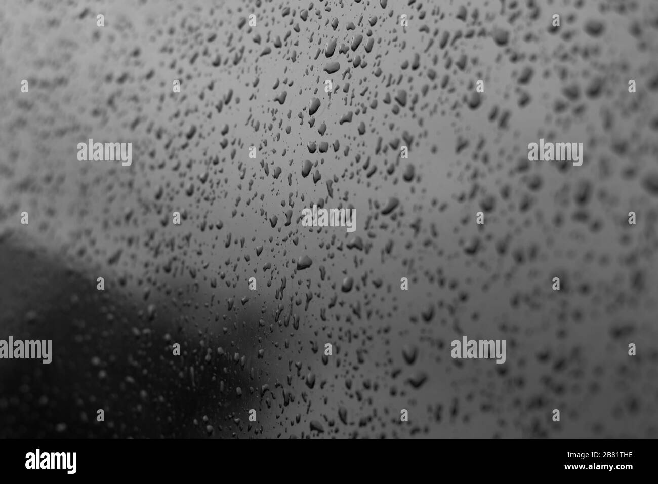 Wassertropfen auf einem Autoglas. Schwarz getöntes Autofenster mit Regentropfen, Spiegelung des klaren Himmels. Textur für das Design. Stockfoto
