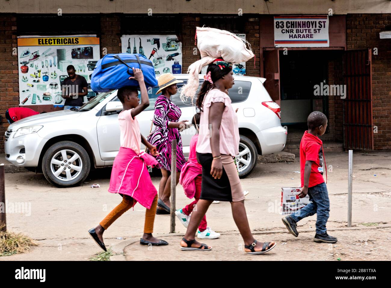 Auf dem Heimweg. Eine Gruppe von Frauen, zwei mit Taschen auf dem Kopf, folgen der Führung eines jungen Sohnes, während sie die Chinhoyi Straße in Harare entlang gehen. Stockfoto