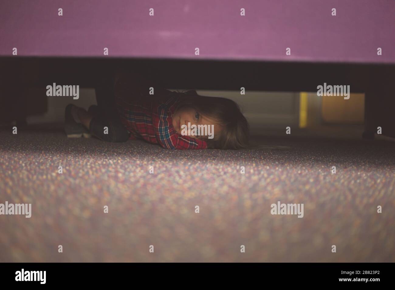 Ein kleiner Vorschulter versteckt sich unter dem Bett Stockfoto