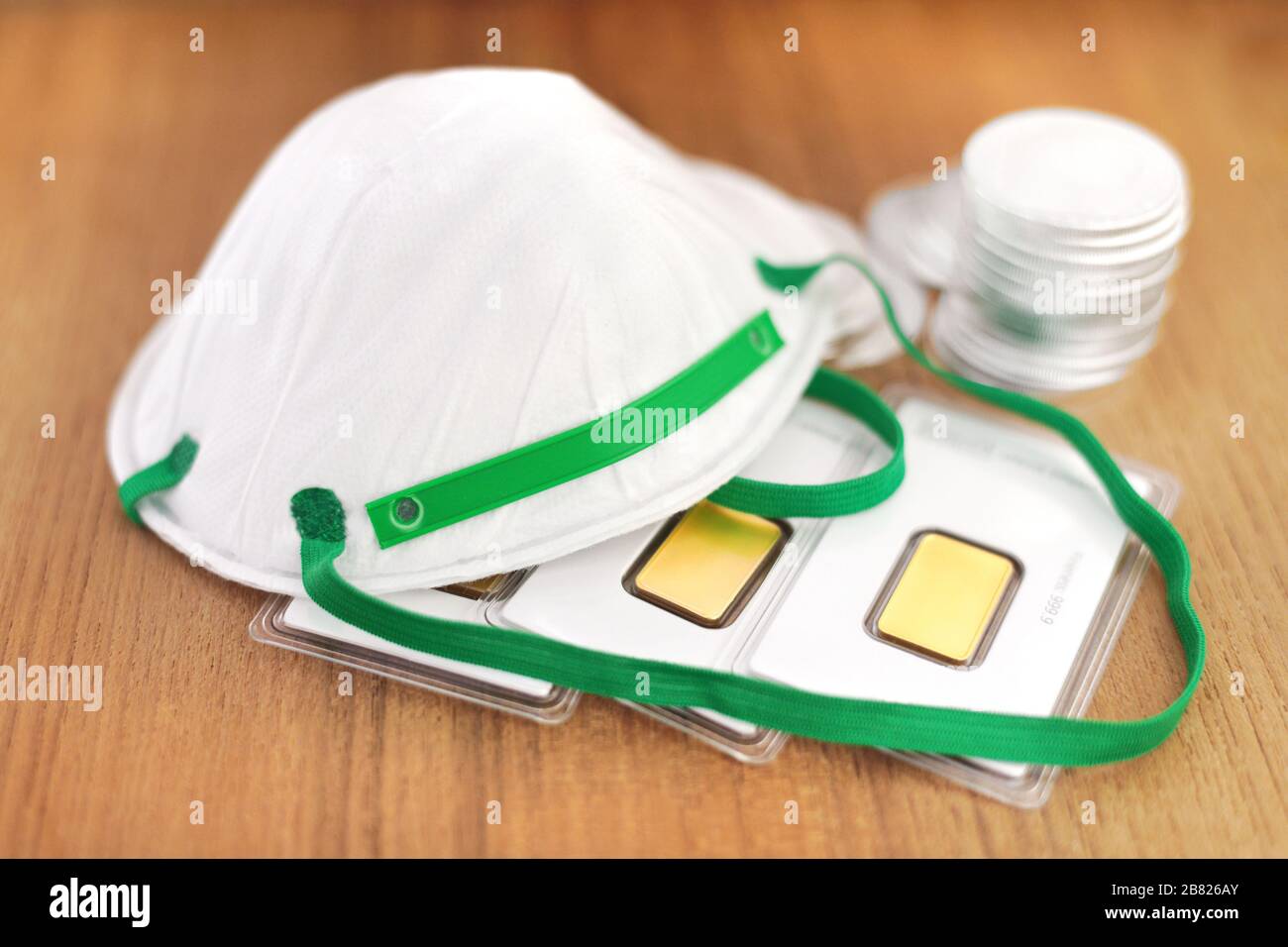 Eine Maske mit Goldbarren und Silbermünzen auf einem Holztisch. Stockfoto