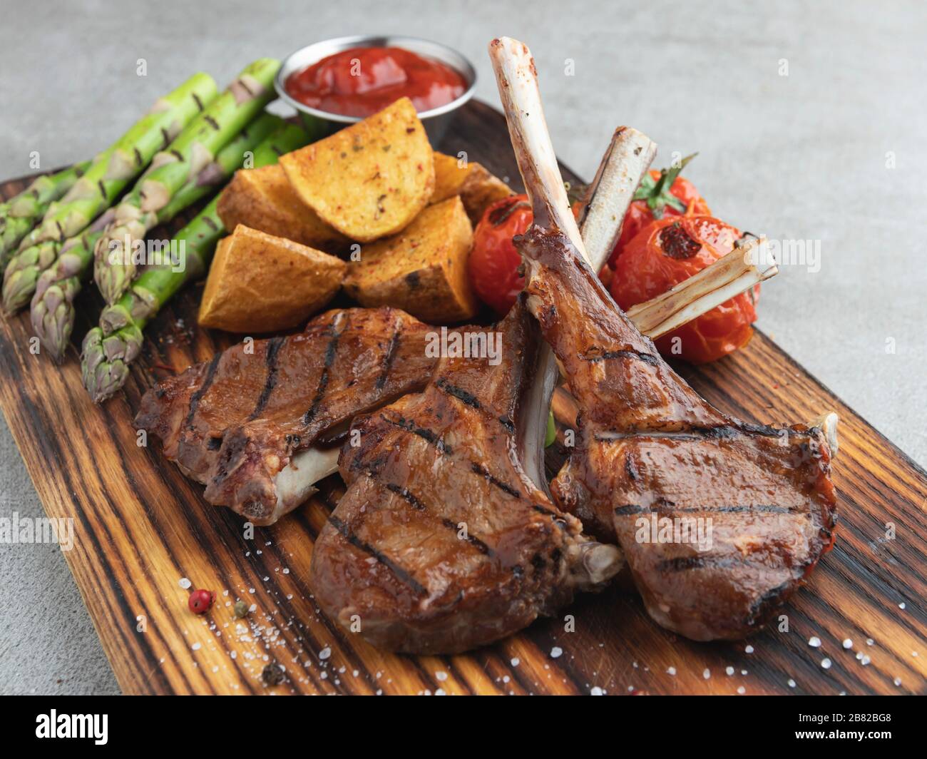 Gegrillte Lammkoteletts auf einem Holzbrett mit Spargel, roter Soße, Kartoffeln Stockfoto