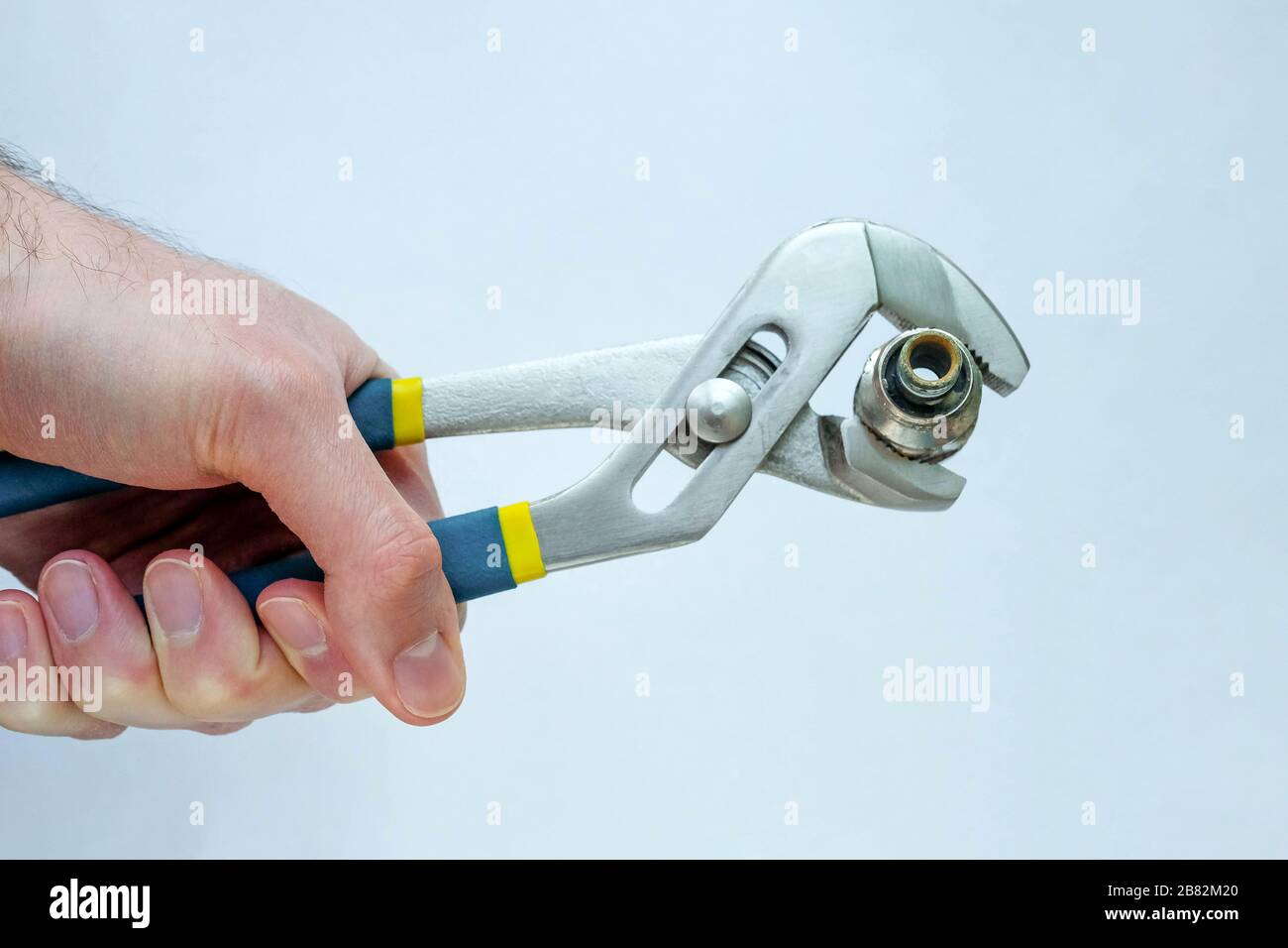 Die Kupplung wird in Zange gespannt. Verstellbarer Schraubenschlüssel. Die Hand hält das Klempnerwerkzeug. Stockfoto