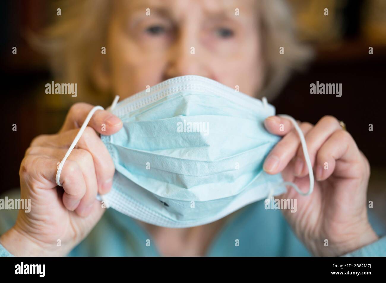 Ältere ältere ältere kaukasische Frau, die eine medizinische prozedurale Gesichtsmaske zum Schutz vor COVID-19, Coronavirus Infektion, aufsetzt Stockfoto