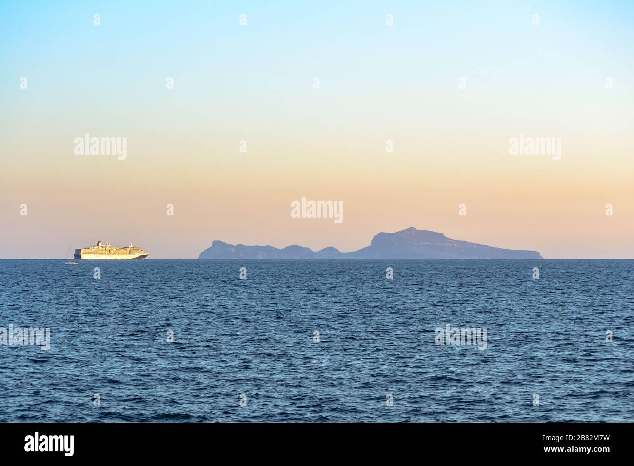 Die Insel Capri am Horizont liegt über dem Golf von Neapel, der von der Küste der Stadt aus gesehen wird, in einem Landschaftsblick bei Sonnenuntergang mit einem großen Schiff langsam navi Stockfoto