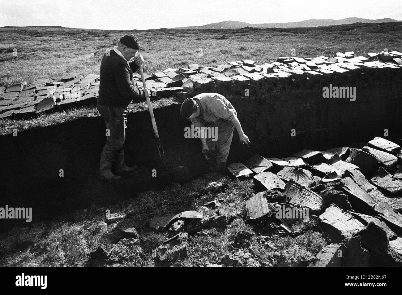 Zwei Männer schneiden Torf auf einem Landstück am Loch Portan auf der Insel North Uist in den äußeren Hebriden, Schottland. Torfschnitt war eine traditionelle Methode, um Brennstoff für den Winter in den dünn besiedelten Gebieten an Schottlands Westküste und Inseln zu sammeln. Der Torf wurde getrocknet und in Bränden und Öfen verwendet. Stockfoto