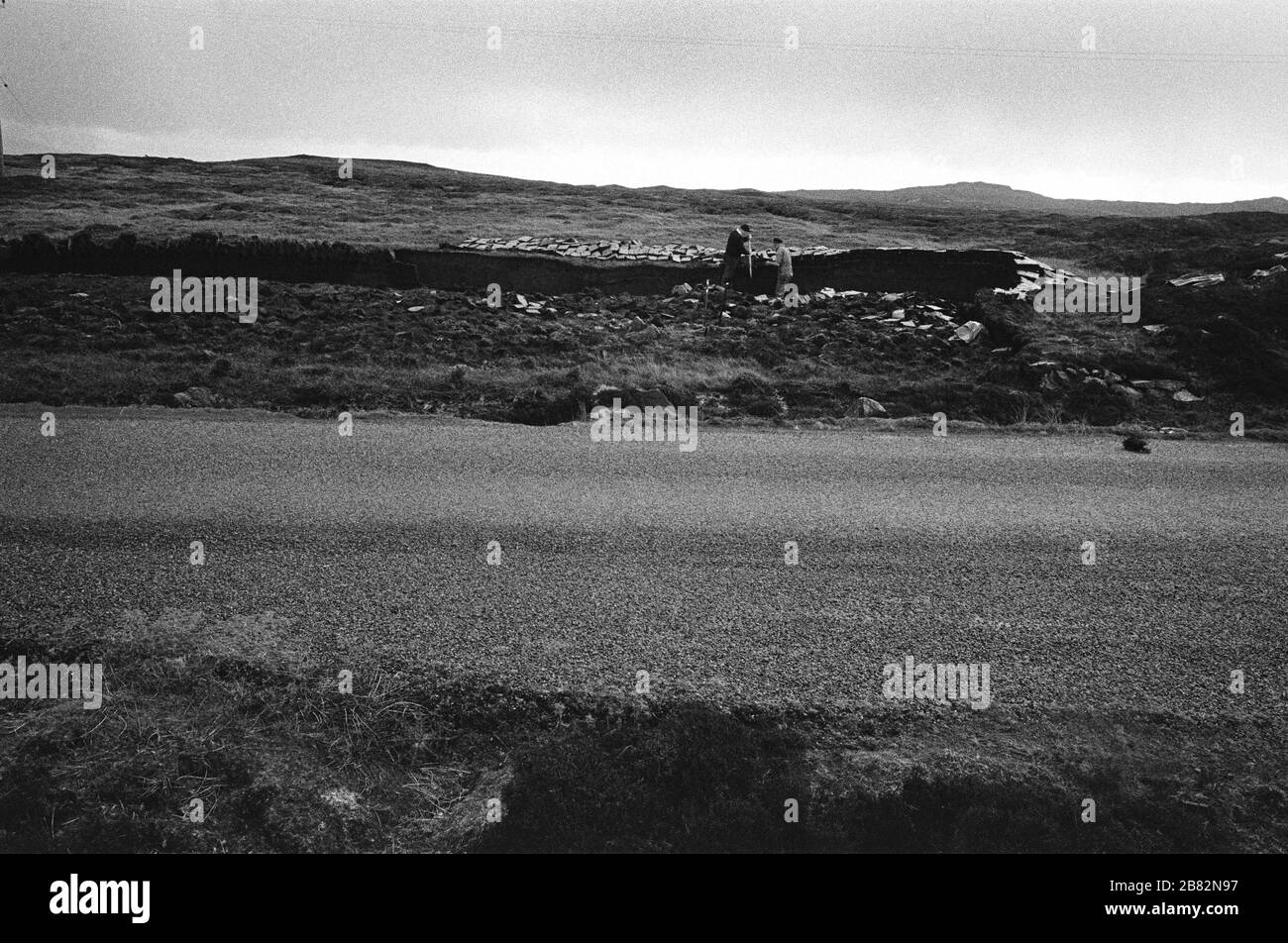 Zwei Männer schneiden Torf auf einem Landstück am Loch Portan auf der Insel North Uist in den äußeren Hebriden, Schottland. Torfschnitt war eine traditionelle Methode, um Brennstoff für den Winter in den dünn besiedelten Gebieten an Schottlands Westküste und Inseln zu sammeln. Der Torf wurde getrocknet und in Bränden und Öfen verwendet. Stockfoto