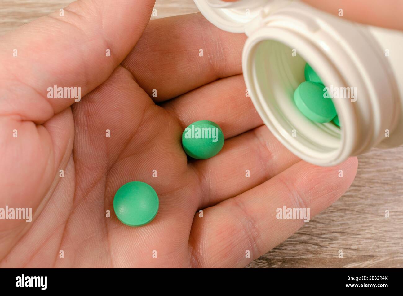 Die menschliche Hand nimmt grüne Pillen aus einem Glas oder einem Behälter. Gesundheit und Medizin. Nahaufnahme. Makro. Stockfoto