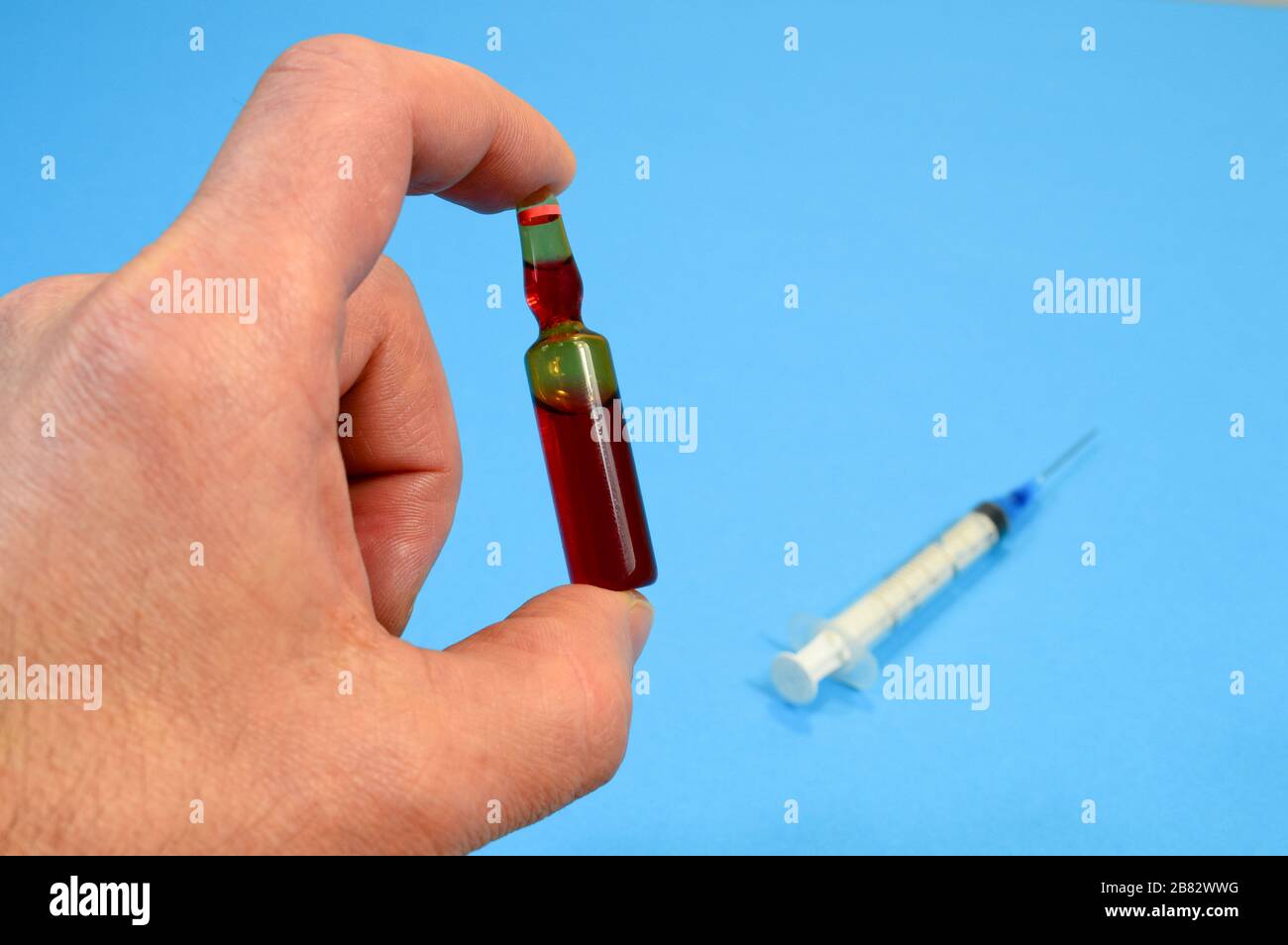 Ampulle mit Impfstoff aus einem neuen Coronavirus in einer menschlichen Hand auf blauem Hintergrund, Grippeimpfungskonzept Stockfoto