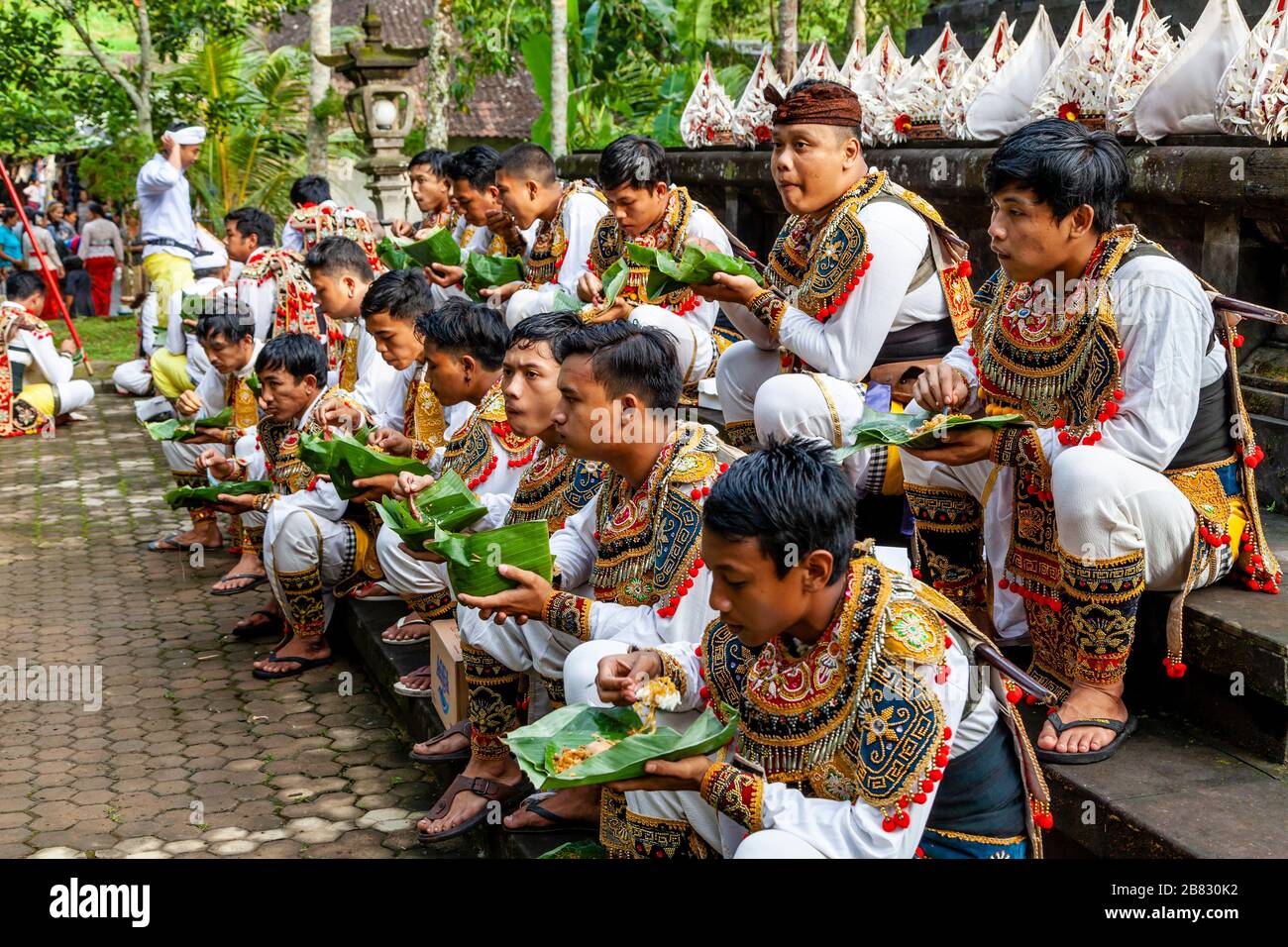 Eine Gruppe junger Männer im Kostüm, die Mittagessen auf EINEM Hindu-Festival, dem Wassertempel von Tyrta Emmul, Bali, Indonesien essen. Stockfoto