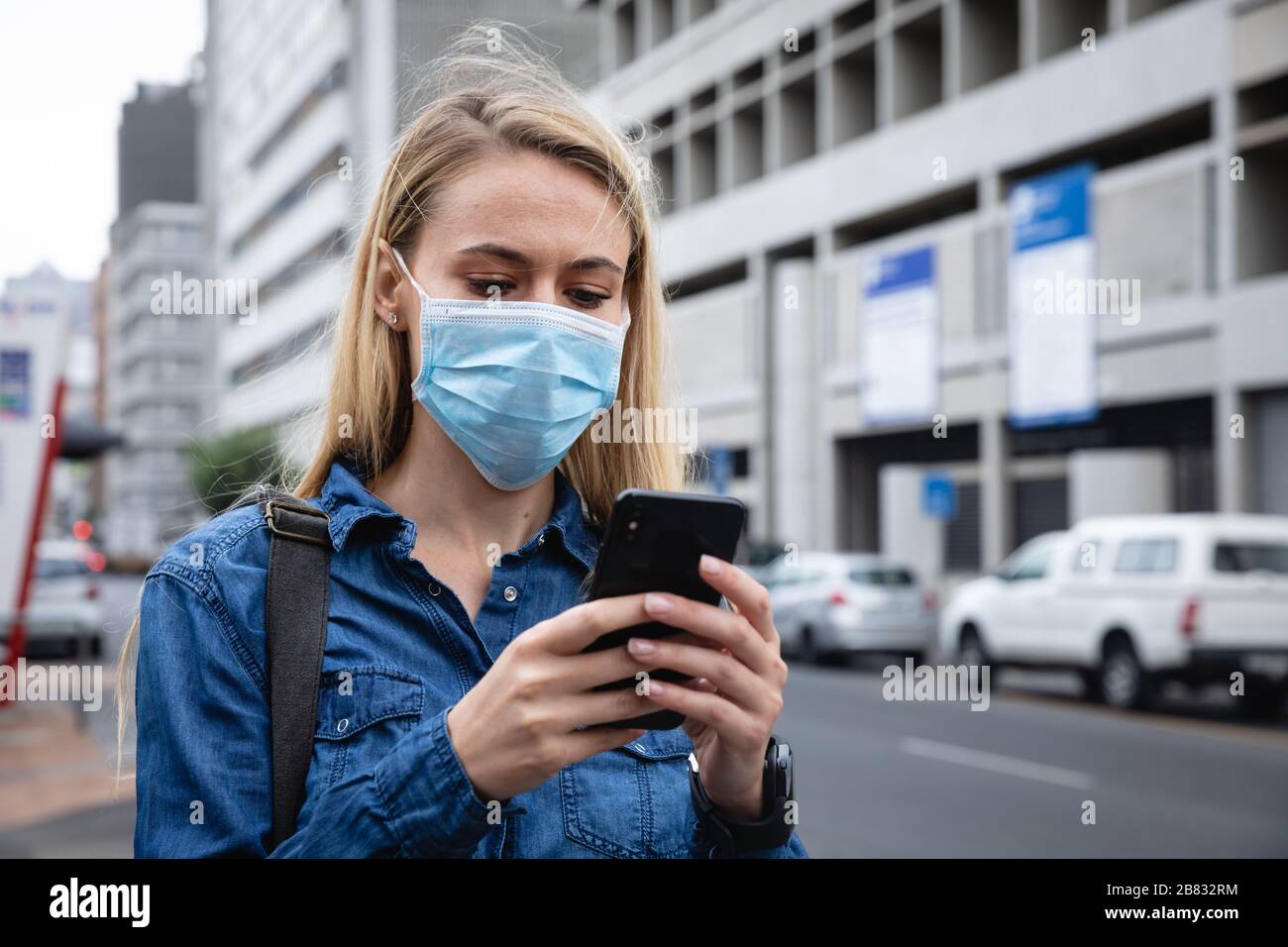 Kaukasische Frau, die eine kovidte 19-Coronavirus-Maske außerhalb und mit ihrem Telefon trägt Stockfoto