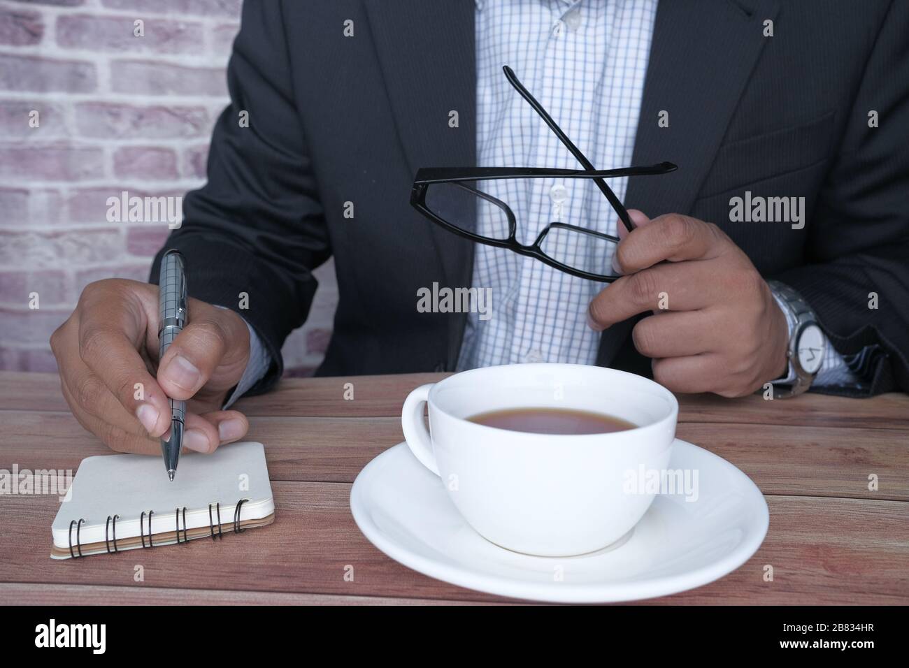 Geschäftsmann, der auf Notizblock am Tisch schreibt Stockfoto