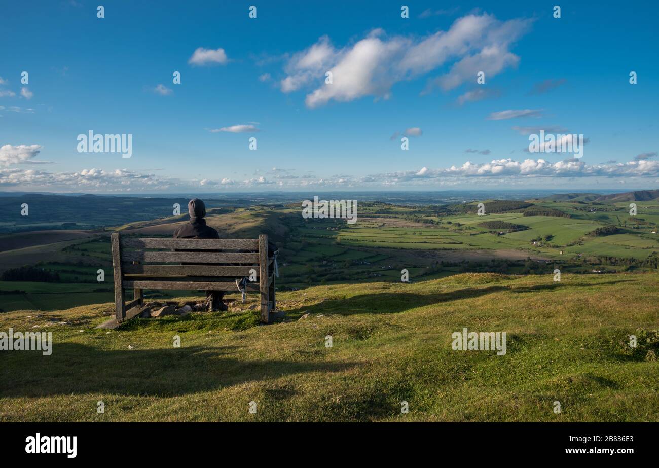 Ein Wanderer sitzt auf einer Bank mit Blick auf die Landschaft von Mid Wales. Corndon Hill, Powys, Wales. Stockfoto