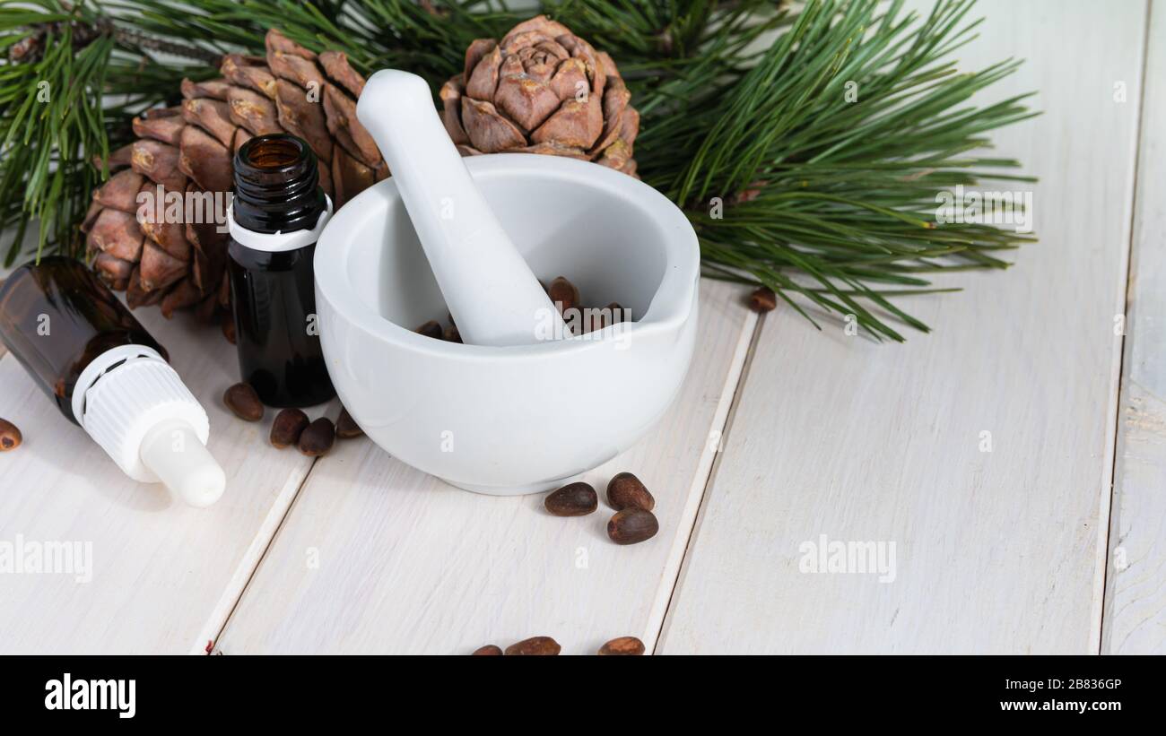 Kiefernkegel mit Nüssen, Mörtel und Glasflasche auf einem weißen Holztisch Organische und gesunde Superfood. Stockfoto