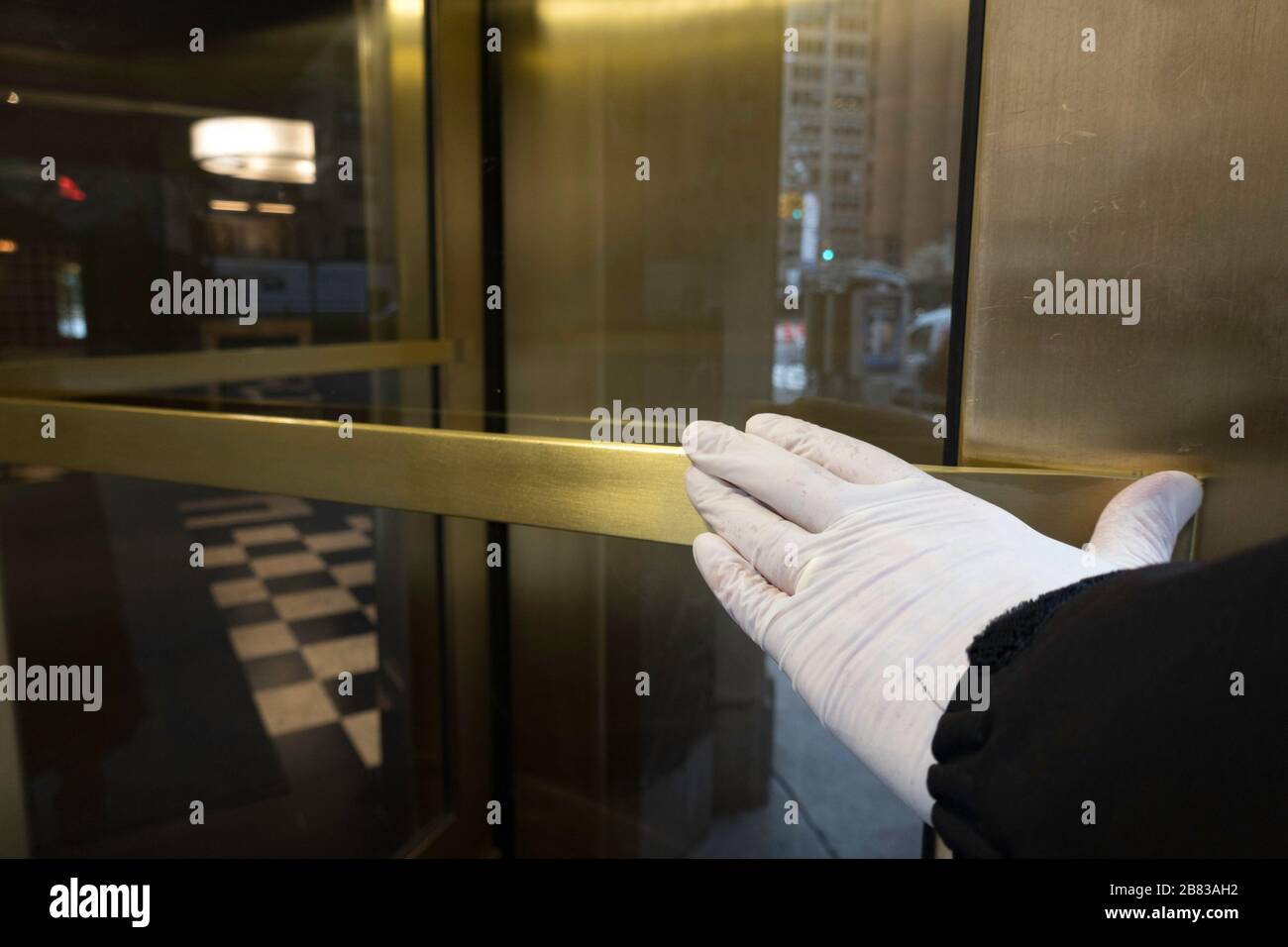 Ein Bewohner von New York City schiebt eine Drehtür mit einer Handschuhhand als Vorsichtsmaßnahme gegen Keime während der COVID-19-Pandemie, USA Stockfoto