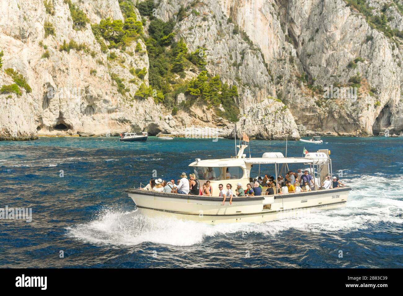 Insel CAPRI, ITALIEN - AUGUST 2019: Gruppe von Menschen an Bord eines Motorboots auf einem Touristenausflug rund um die Insel Capri. Stockfoto