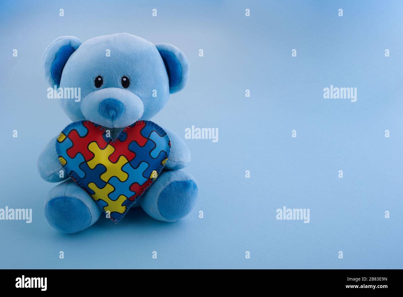 World Autism Awareness, Konzept mit Teddybären, das Puzzle oder Puzzle-Muster auf Herz auf blauem Hintergrund hält Stockfoto