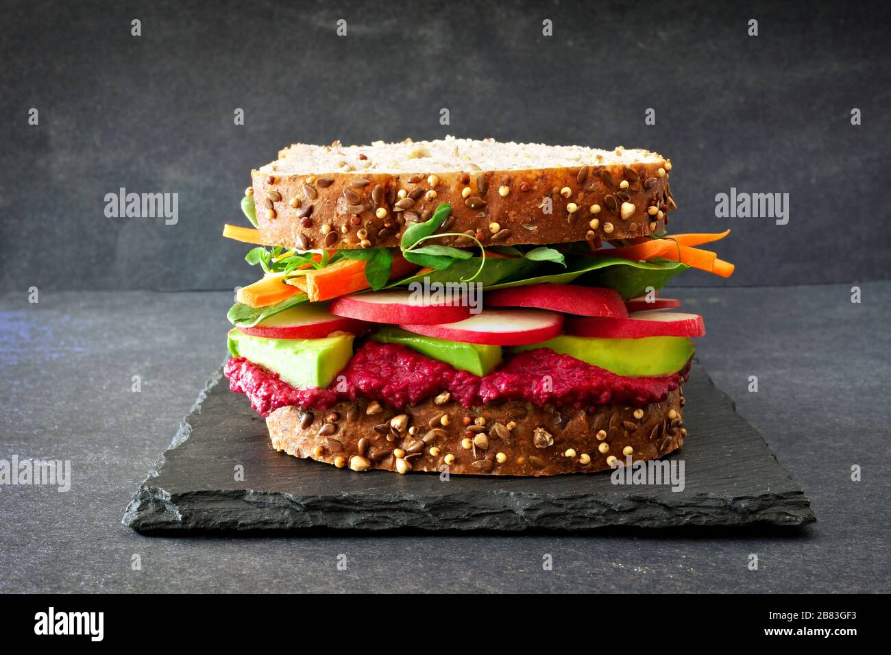 Superfood Sandwich mit Zuckerrüben Hummus, Avocado, Gemüse und Grüns, auf Vollkornbrot gegen einen Schiefer Hintergrund Stockfoto