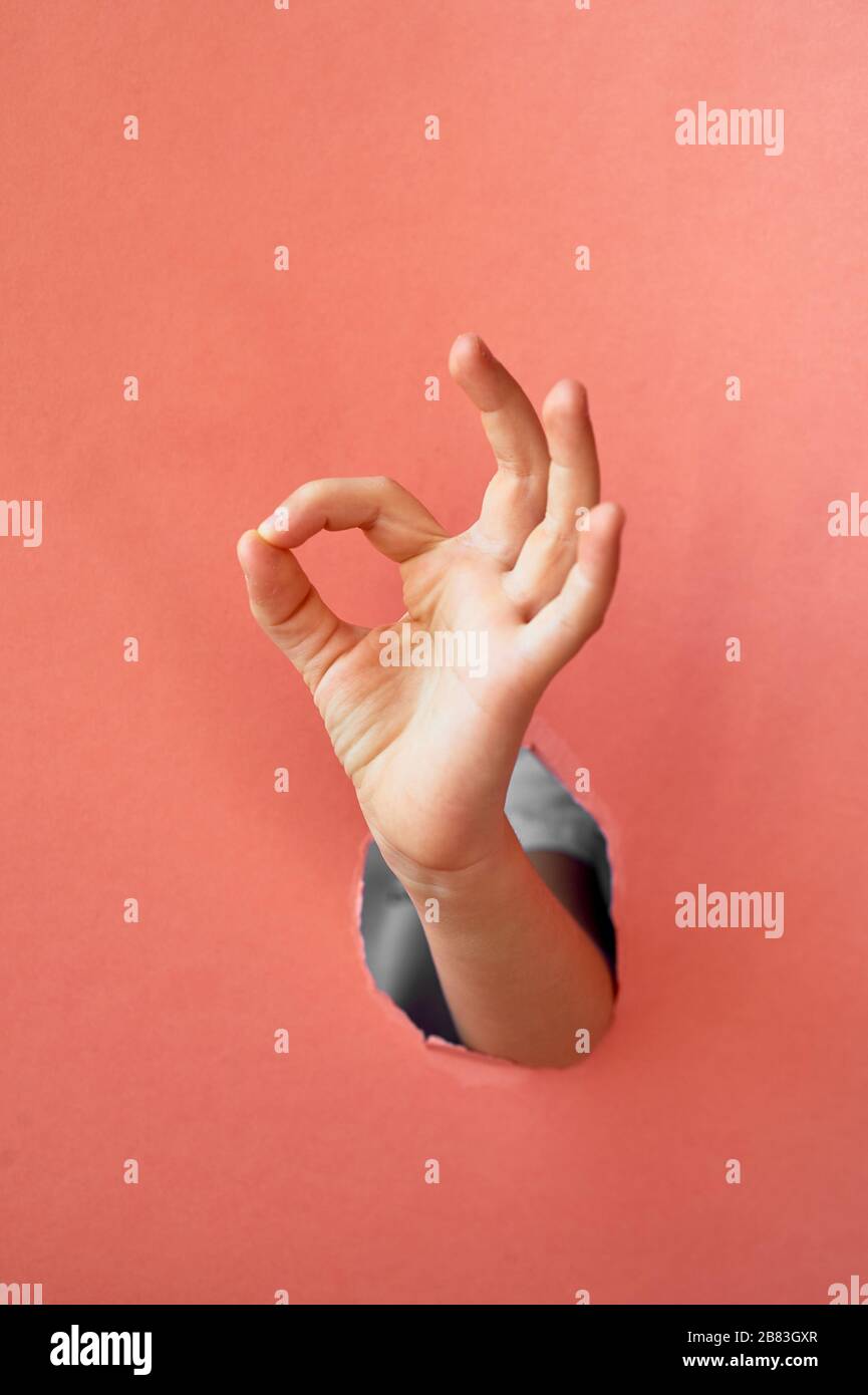 Die Hand eines Kindes macht ein Zeichen, alles wird gut, OK.Trend Hand in einem Loch aus rosa Papier. Stockfoto