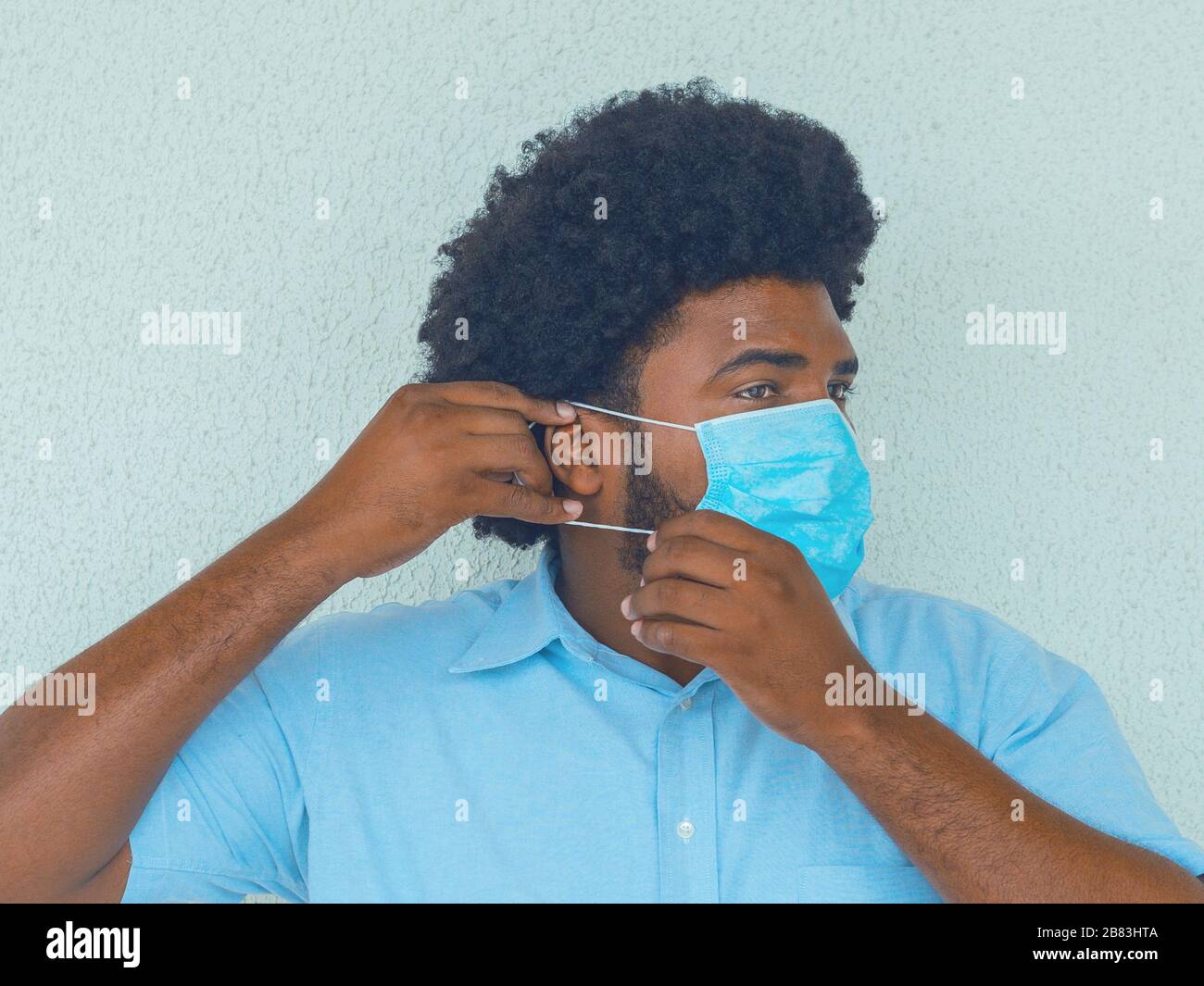 Ein Mann in einem blauen Hemd, der eine medizinische Maske aufsetzt, um ein Contagio zu vermeiden Stockfoto