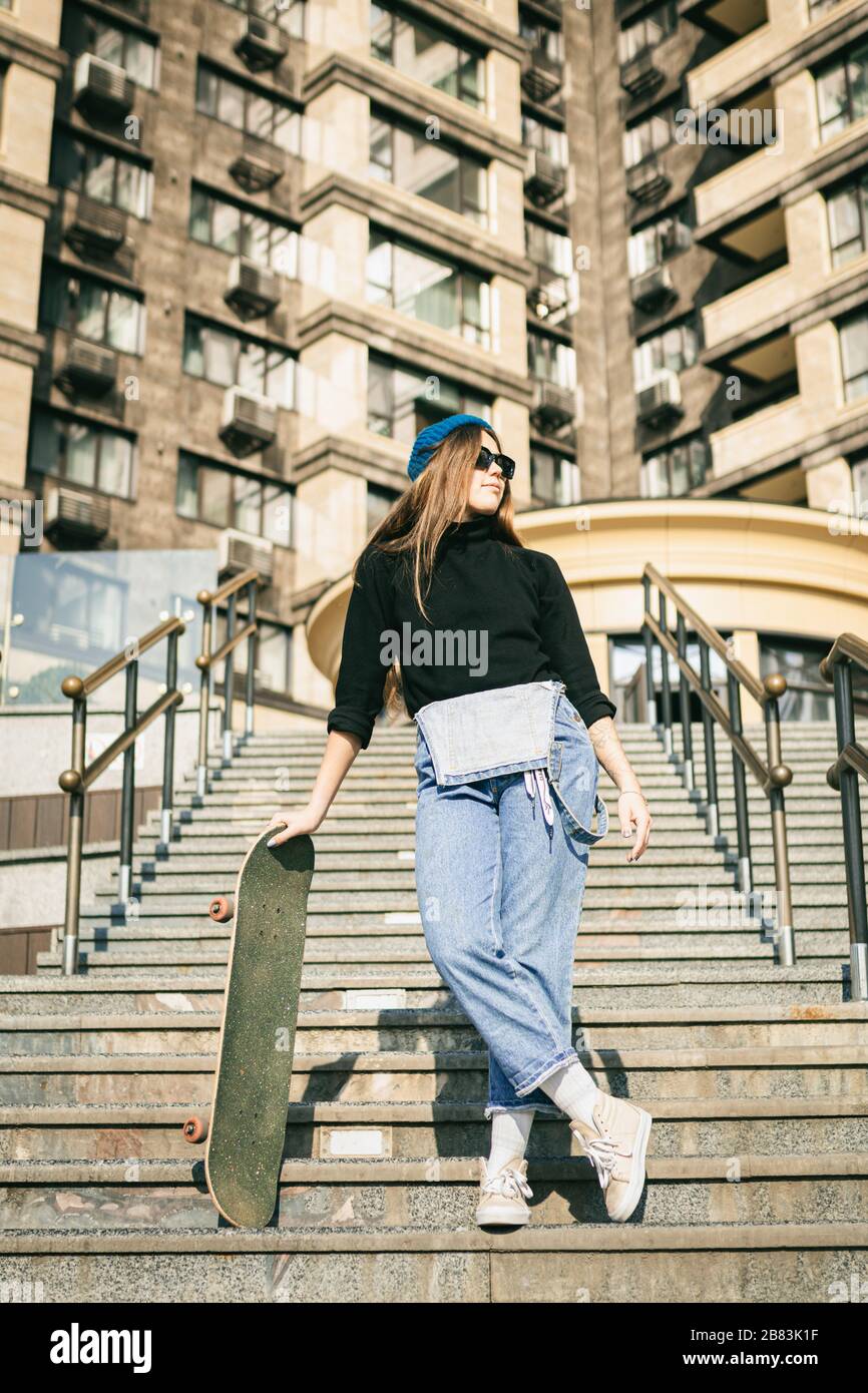 Urbane Frau mit Skate. Hipper-Mädchen mit Skateboard in der Stadt. Konzept für Extremsport und Emotionen. Alternativer Lebensstil. Modische Hüftmädchenhaltung Stockfoto