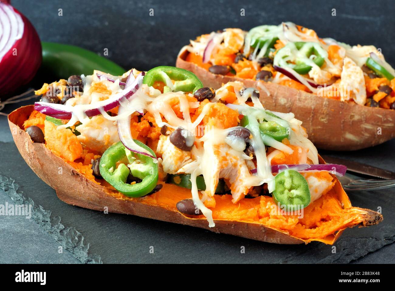 Gebackene Süßkartoffeln mit Huhn, Gemüse und Käse, dicht auf dunklem Hintergrund Stockfoto