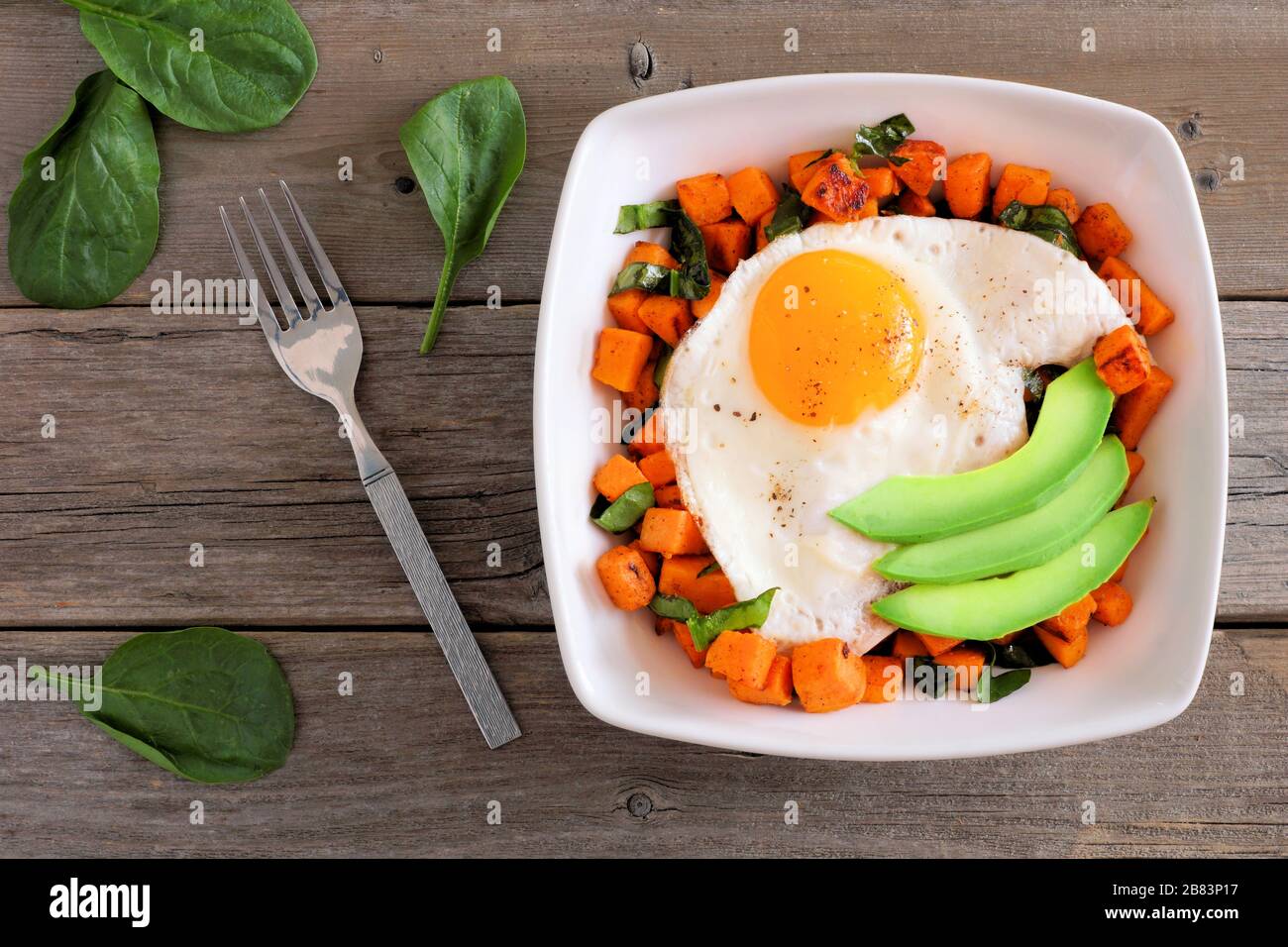 Nährstoffschüssel mit Süßkartoffel, Ei, Avocado und Spinat über der Szene auf rustikalem Holz Stockfoto