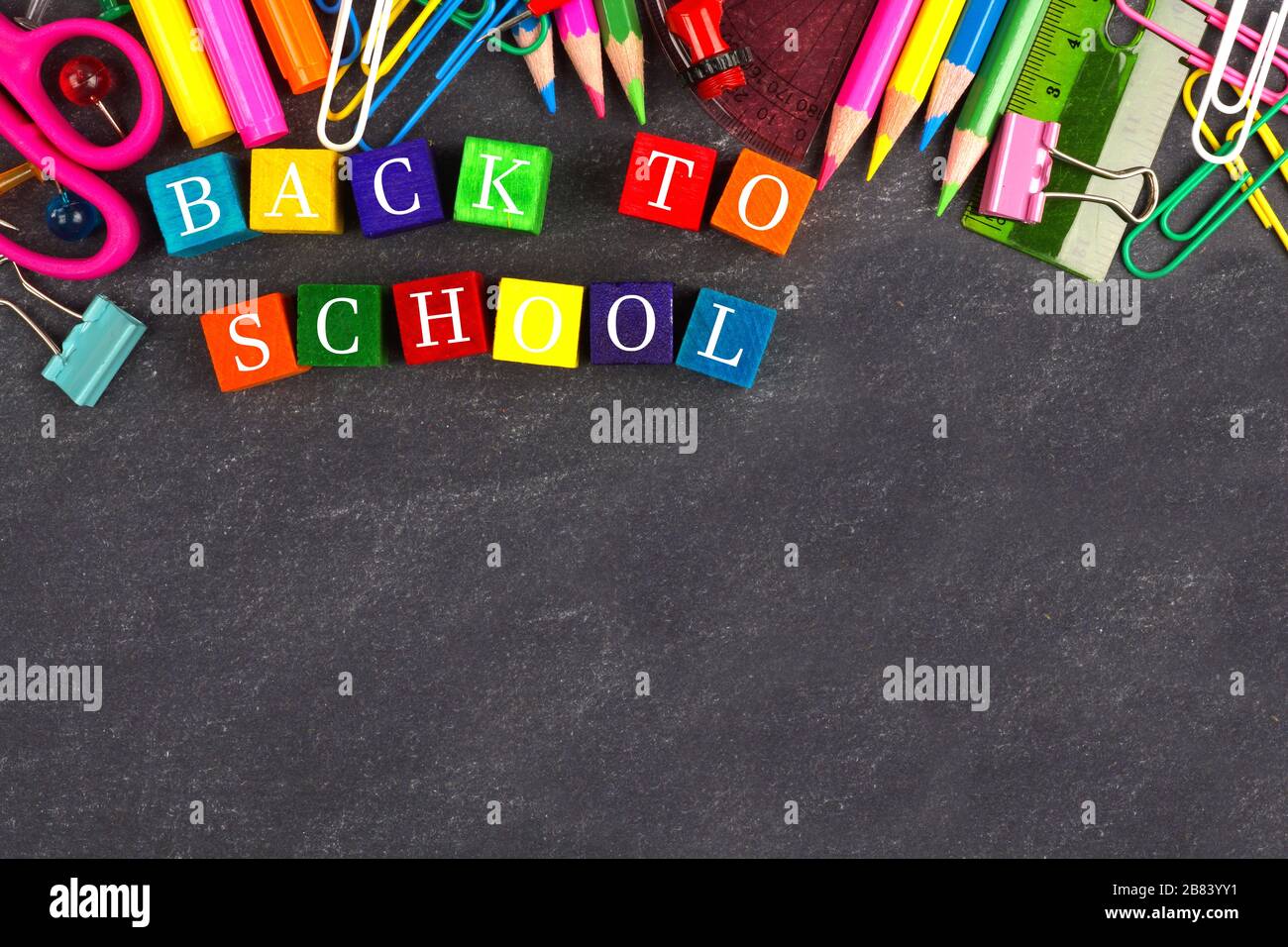 Bunte Back-to-School Holzblöcke mit Schulbedarf obere Grenze auf einem Schwarzen Brett Stockfoto
