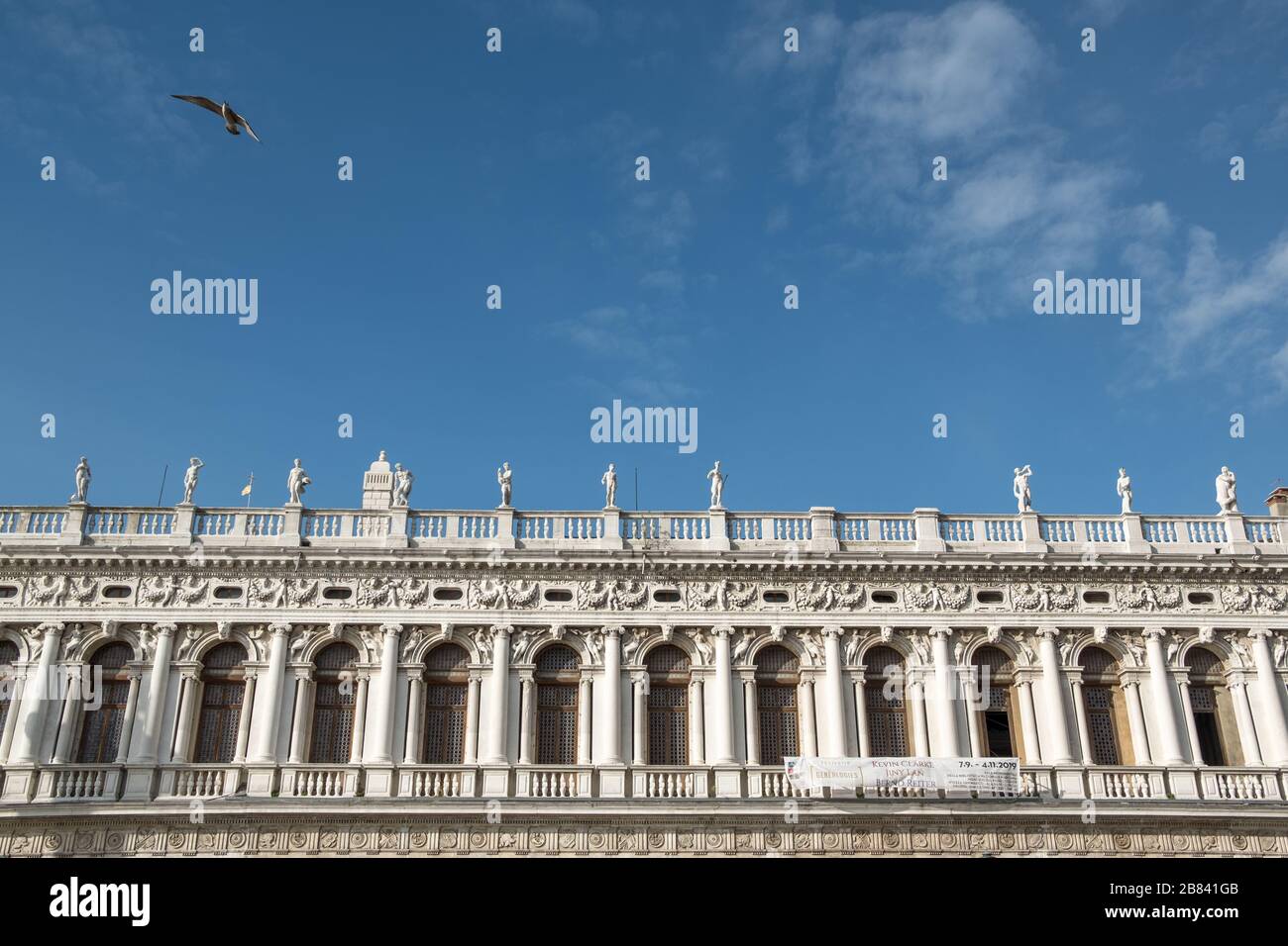 Verzierte obere Etage mit Bögen, Säulen, Statuen und Balkons. Markusplatz, Venedig, Italien. Das meiste Bild ist blauer Himmel mit einem Vogel Stockfoto