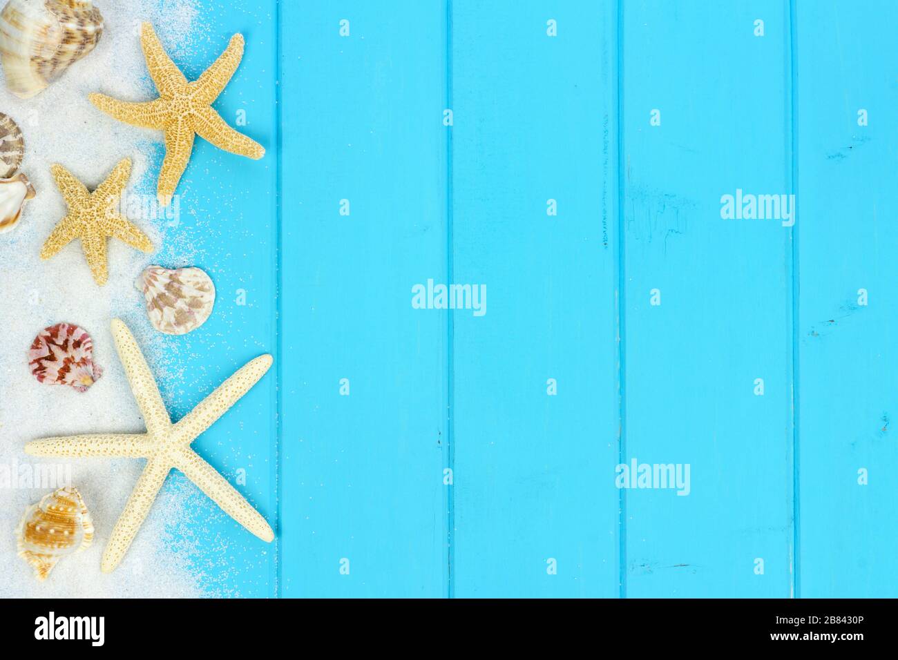 Sommerliche Seitengrenze von Sand, Meeresschalen und Sternenfischen auf blauem Holzgrund Stockfoto