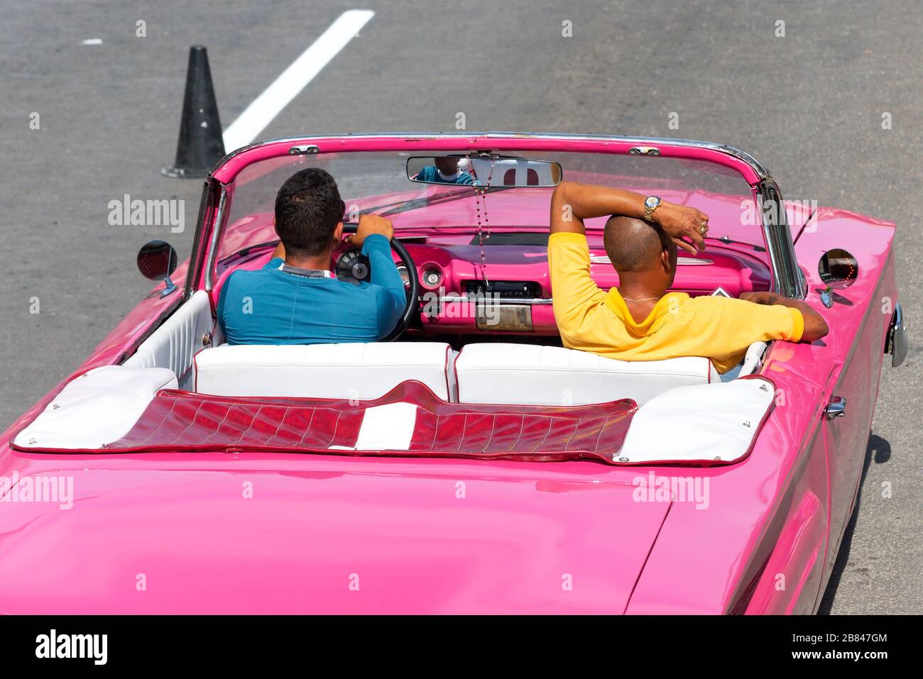 Zwei entspannte kubaner in einem rosafarbenen Oldtimer. Die Fahrt mit einem Oldtimer ist eine der wichtigsten Touristenattraktionen von La Habana/Havanna, Kuba. Blick von hinten. Stockfoto