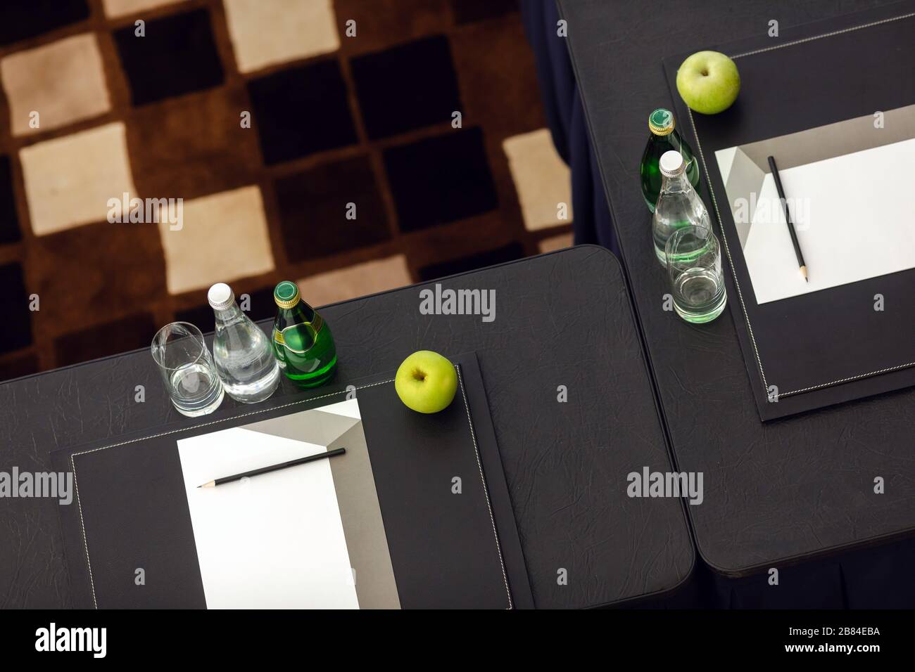 Arrangierte Schreibtische mit Wasser und apfel neben Schreibwaren in der Klasse Stockfoto