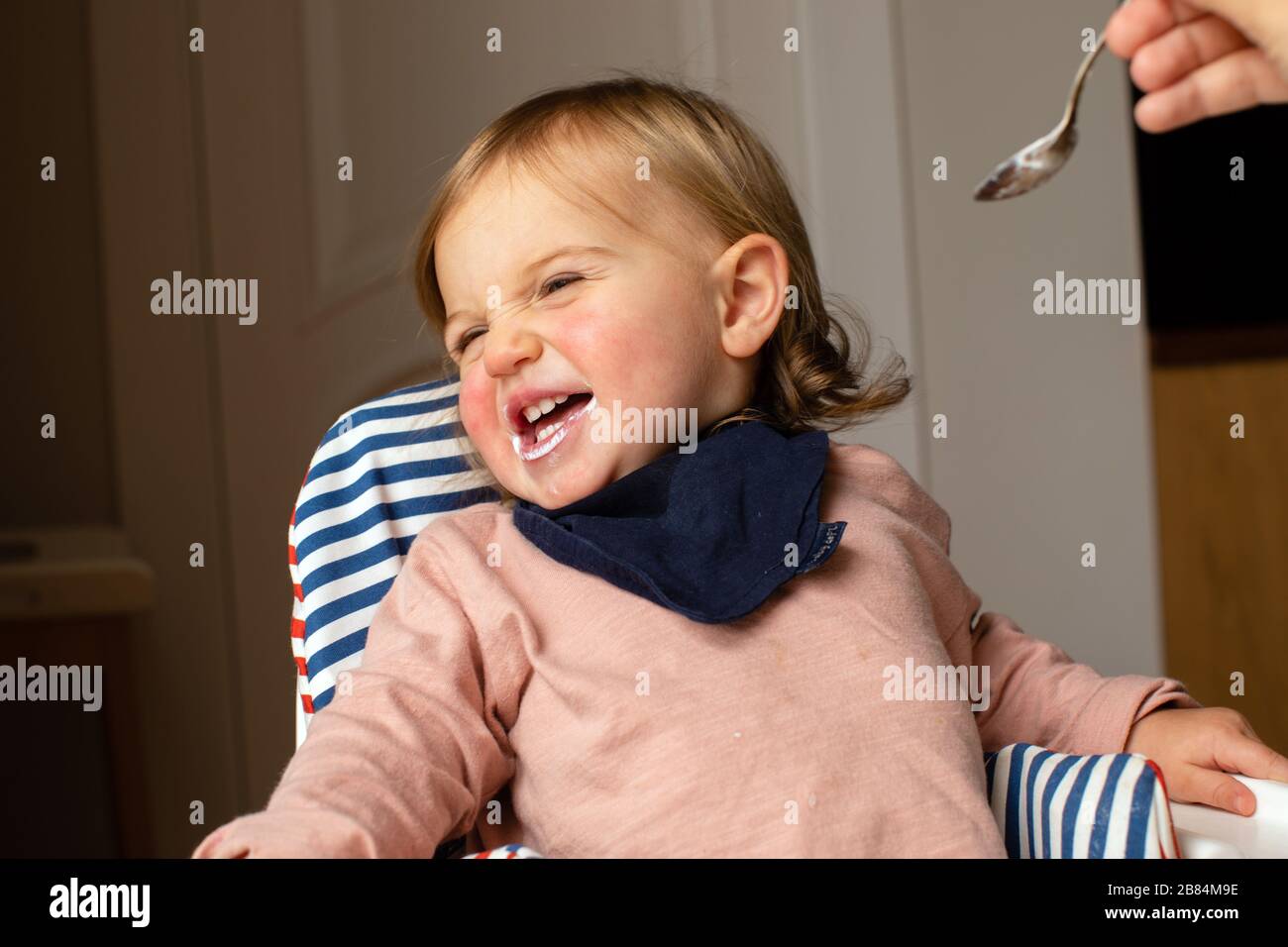 Person, die Kind im Hochstuhl mit abgewendtem Kopf füttert Stockfoto