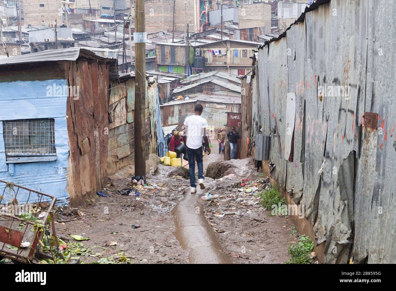 Menschen, die auf einer mit Müll übersäten Gasse von einer Fußgängerbrücke über den Mathare-Fluss, Mathare, Nairobi, Kenia, spazieren gehen. Der Mathare River, einer von Stockfoto