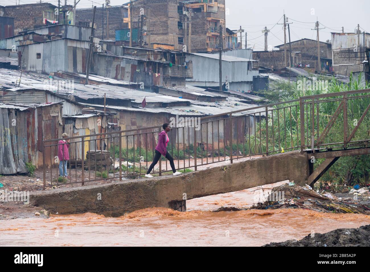 Menschen, die eine Fußgängerbrücke zum Überqueren des Flusses Mathare, Mathare, Nairobi, Kenia benutzen. Der Mathare River, einer der Nebenflüsse des Nairobi River Basi Stockfoto