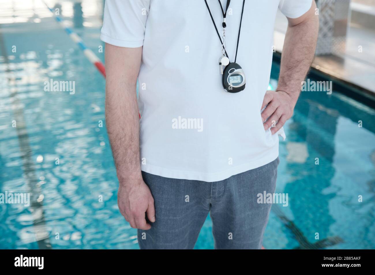 Nahaufnahme unerkennbarer Schwimmtrainer mit Stoppuhr und Pfeifen auf der Brust stehend mit Hand an der Hüfte Stockfoto