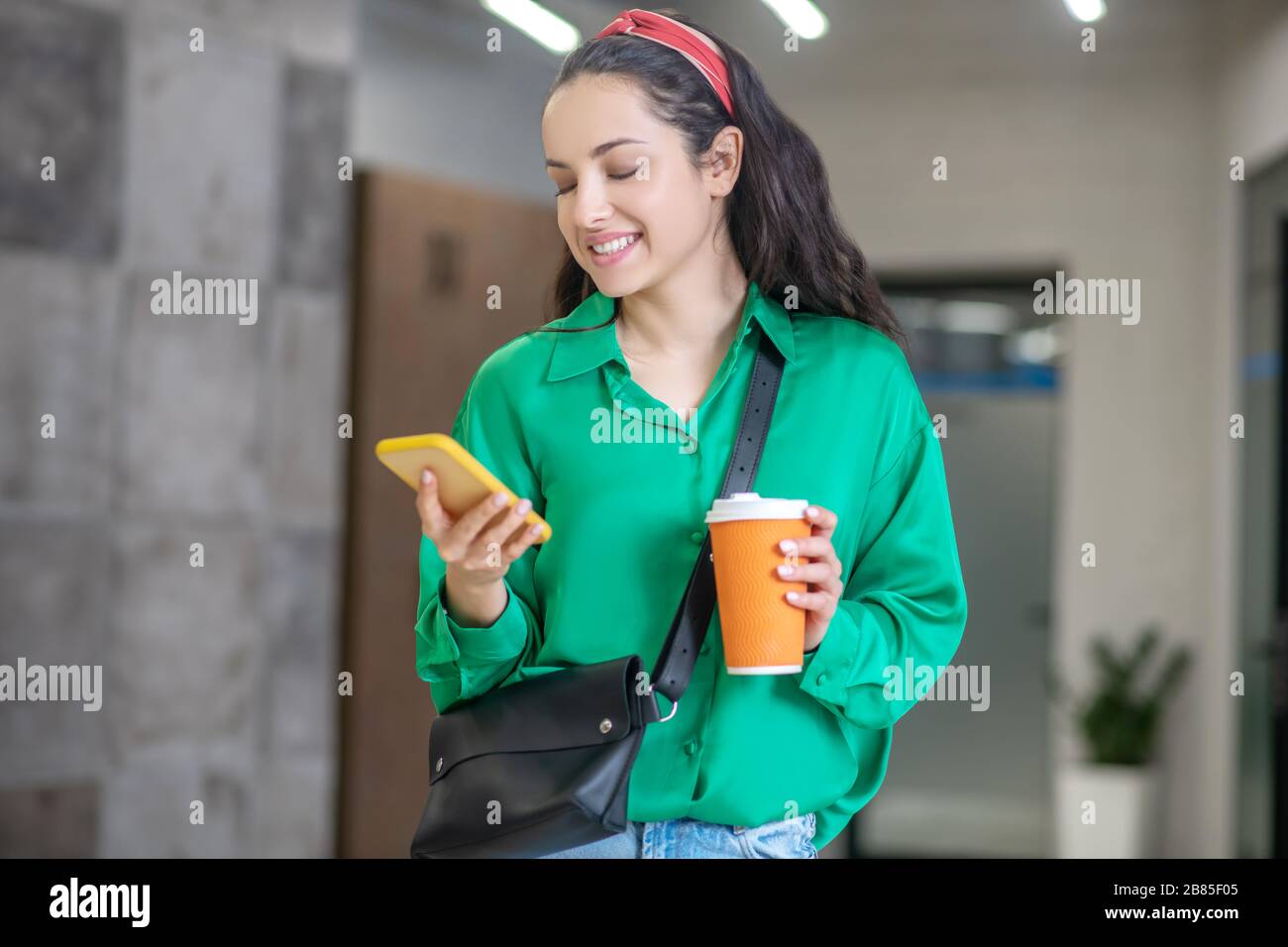 Frau, die im Flur steht und auf das Smartphone blickt. Stockfoto