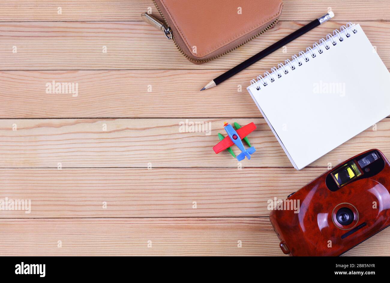 Reisekonzept. Leerer Notizblock mit schwarzem Bleistift, Filmkamera, mit Spielzeugflugzeug und beigefarbener Reißverschlusstafel auf einem Holztisch. Es gibt Platz für Stockfoto